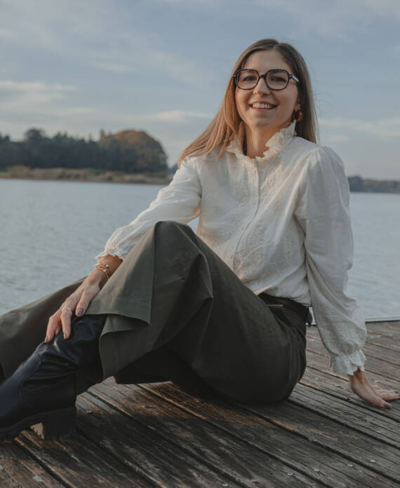 Portrait femme souriante assise sur un ponton en bois au-dessus d'un lac, lors d’une séance portrait à La Roche-sur-Yon en Vendée, réalisée par Solène photographe.