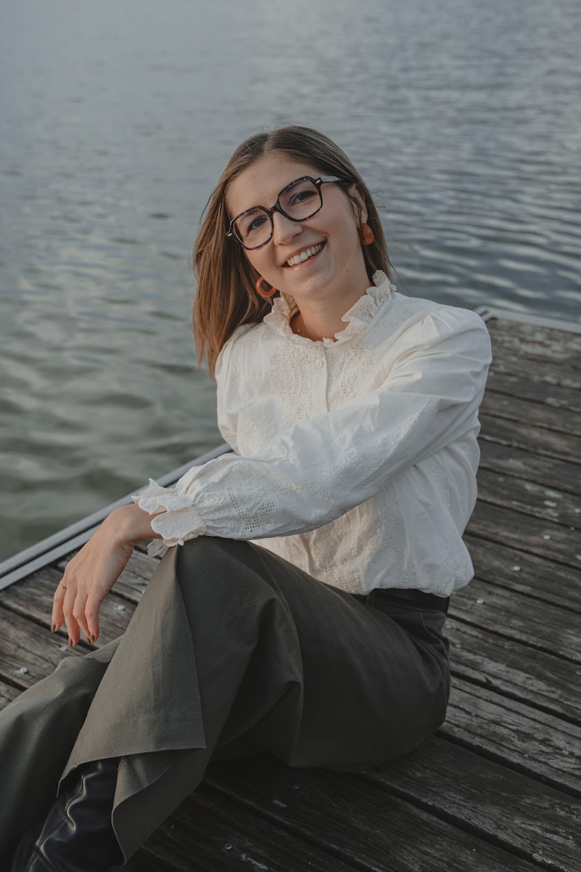Portrait d’une femme souriante assise sur un ponton en bois au-dessus d'un lac avec son bras posé sur une jambe pliée, lors d’une séance portrait à La Roche-sur-Yon en Vendée, réalisée par Solène photographe.