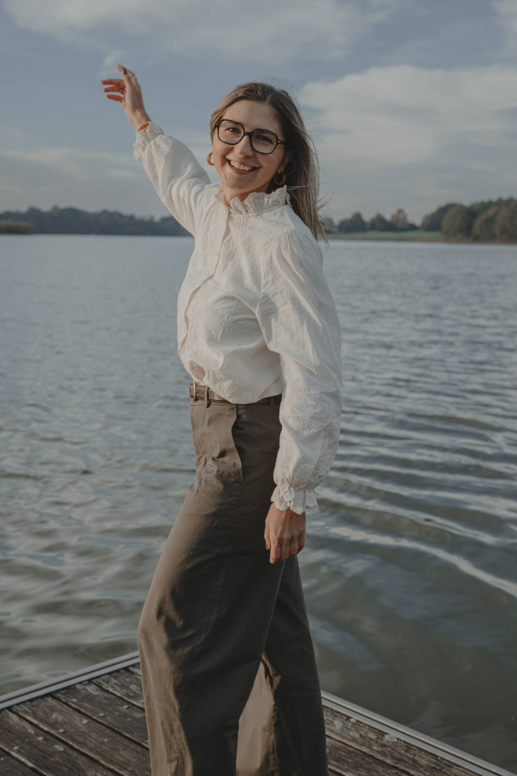 Portrait d’une femme debout sur un ponton en bois au-dessus d’un lac, un bras levé, lors d’une séance portrait à La Roche-sur-Yon en Vendée, réalisée par Solène photographe.