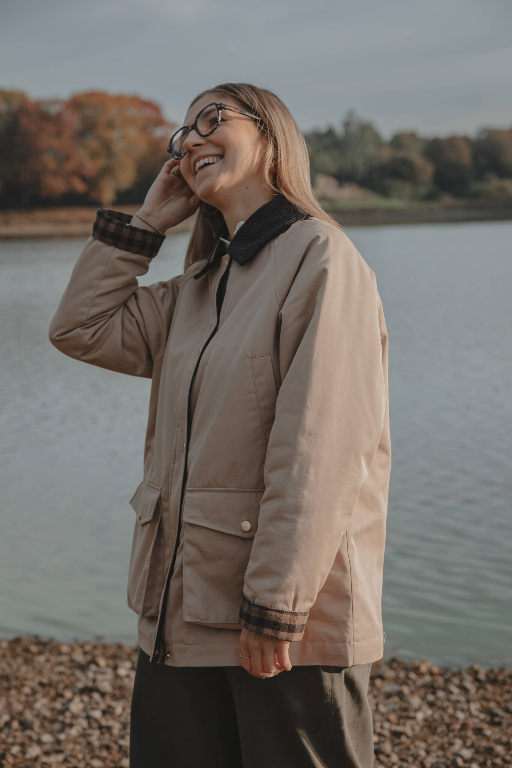 Portrait femme souriante se passant la main dans les cheveux debout près d'un lac, lors d’une séance portrait à La Roche-sur-Yon en Vendée, réalisée par Solène photographe.