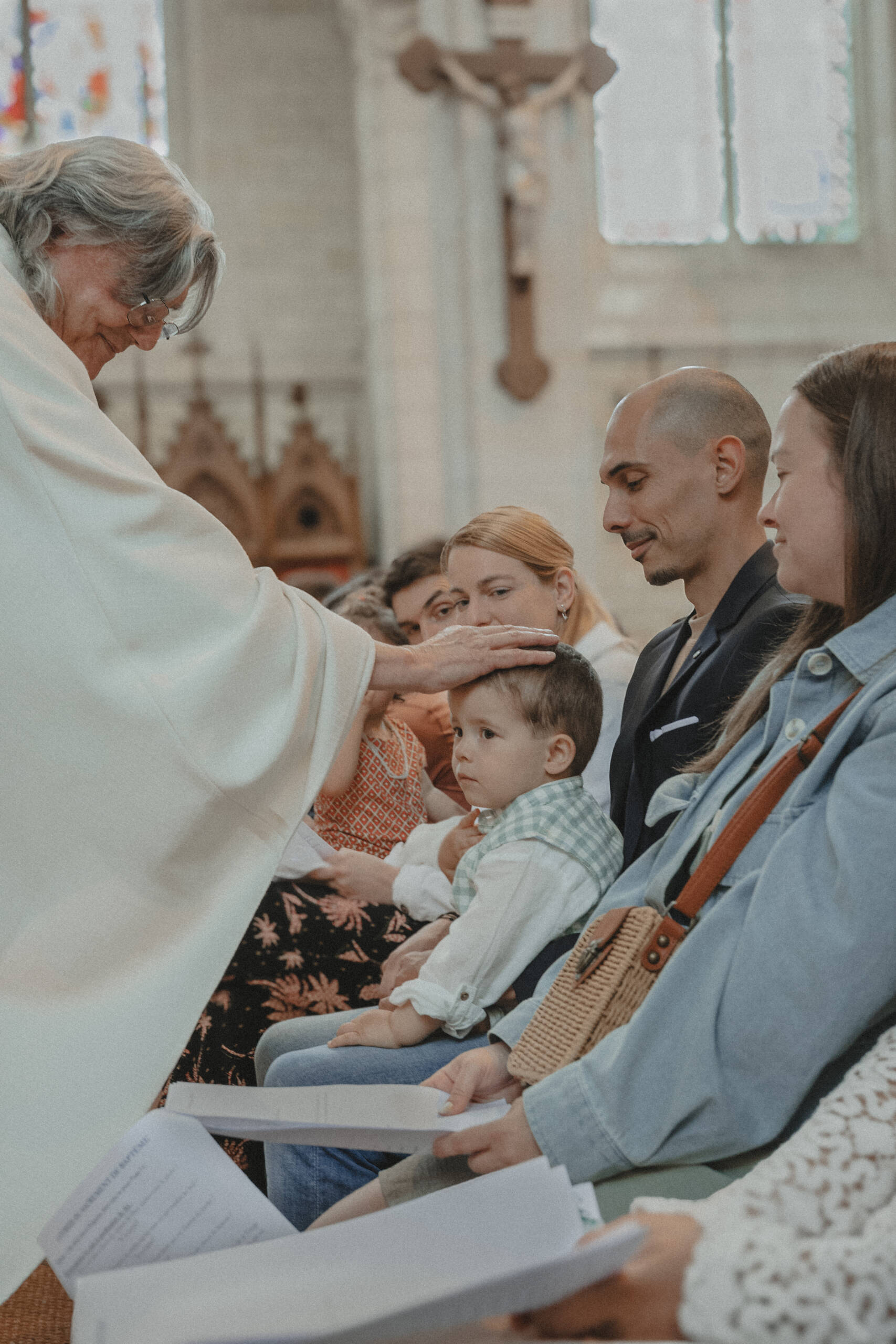 Prêtre posant la main sur la tête d’un enfant lors de son baptême à l’église de L’Herbergement en Vendée. Image réalisée par Solène photographe.