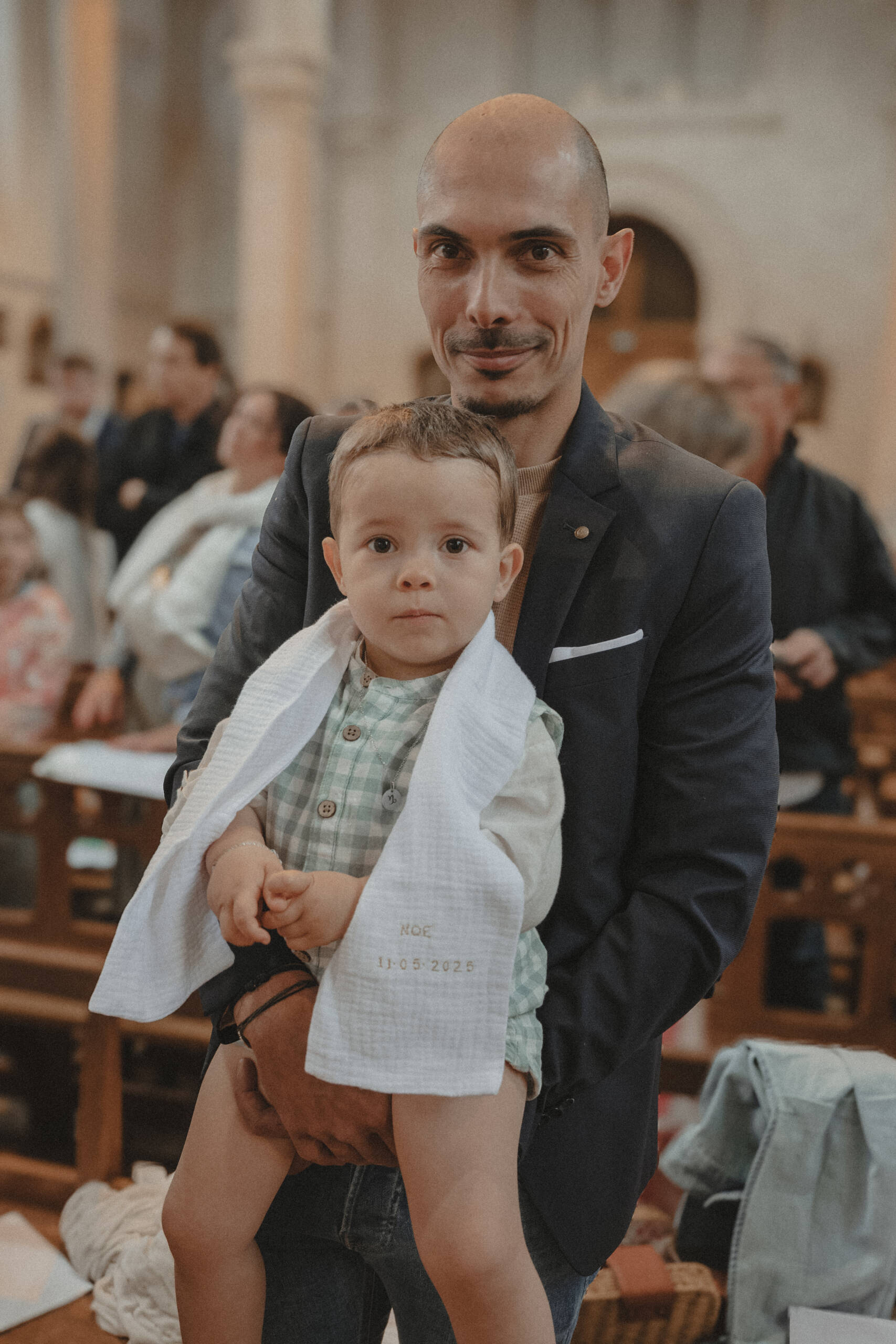 Enfant portant son étole blanche de baptême, dans les bras de son père lors de son baptême à l'église de L'Herbergement en Vendée. Image réalisée par Solène photographe.