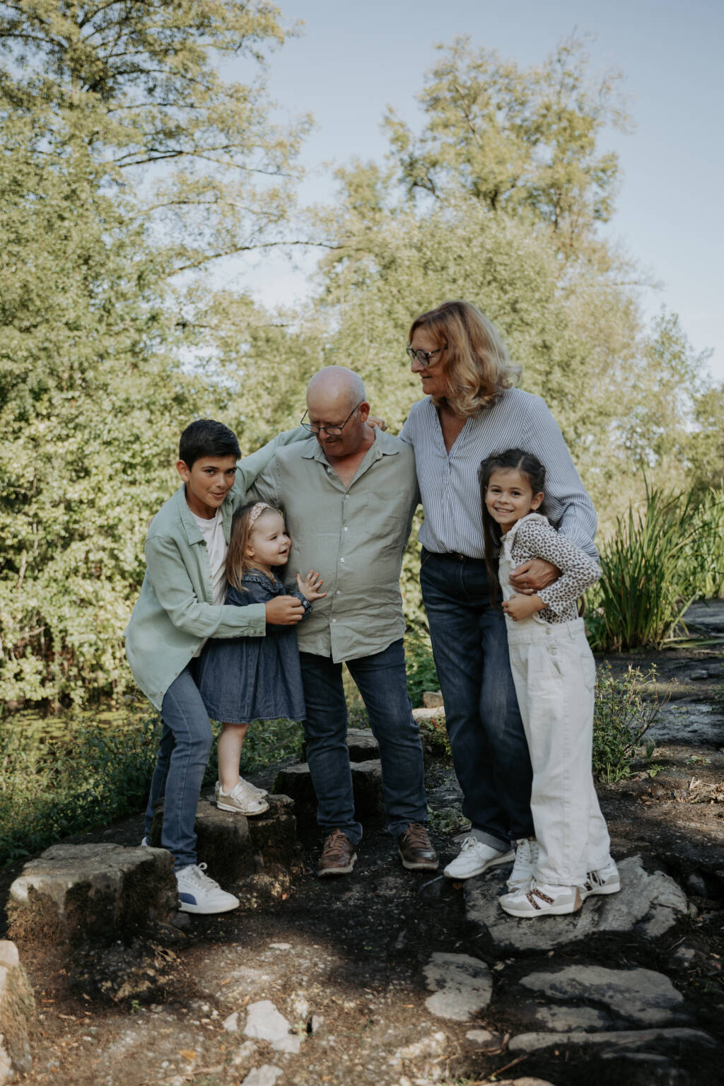 Grands-parents faisant un câlin à leurs petits-enfants sur une digue lors d’une séance photo famille à la Maison de la Rivière à Saint-Georges-de-Montaigu en Vendée, réalisée par Solène photographe.