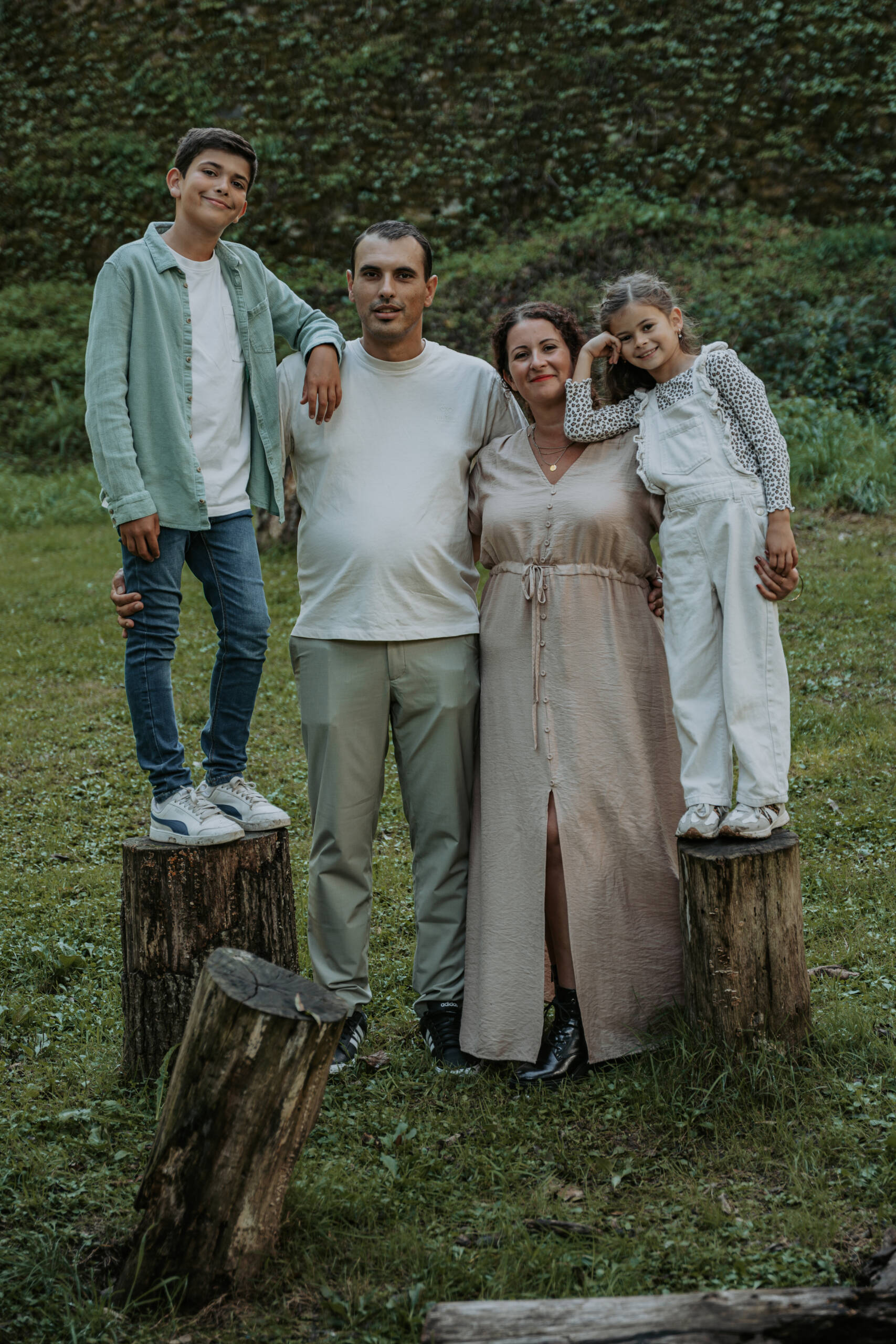 Parents avec leurs deux enfants debout sur des souches d'arbre lors d’une séance photo famille à la Maison de la Rivière à Saint-Georges-de-Montaigu en Vendée, réalisée par Solène photographe.