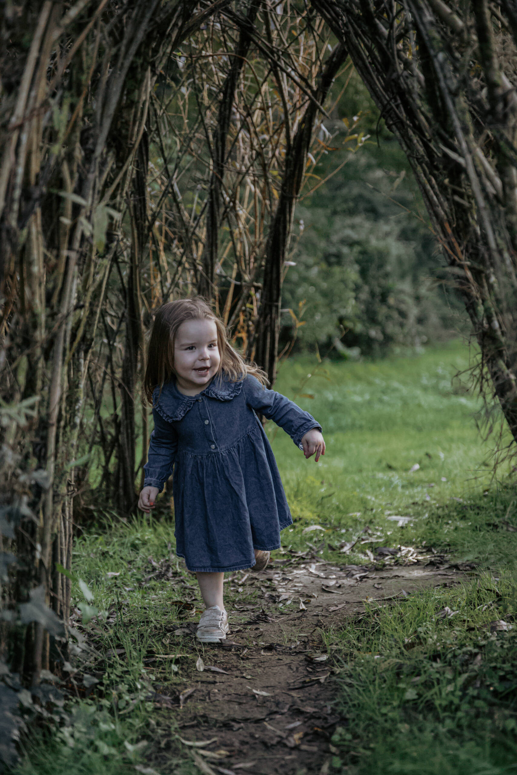 Moment de jeu d'une petite fille capturé sous une arche végétale lors d’une séance photo famille à la Maison de la Rivière à Saint-Georges-de-Montaigu en Vendée, réalisée par Solène photographe.