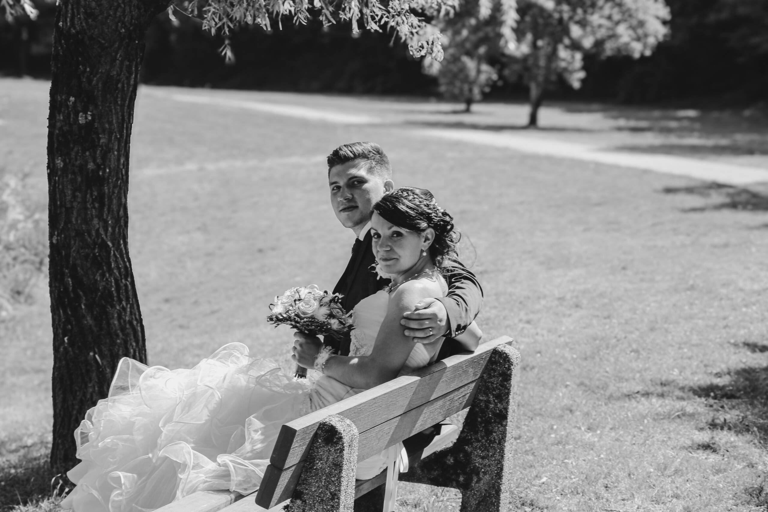 Couple de mariés enlacé sur un banc, lors des photos de couple pendant leur mariage, réalisée en noir et blanc par Solène photographe.