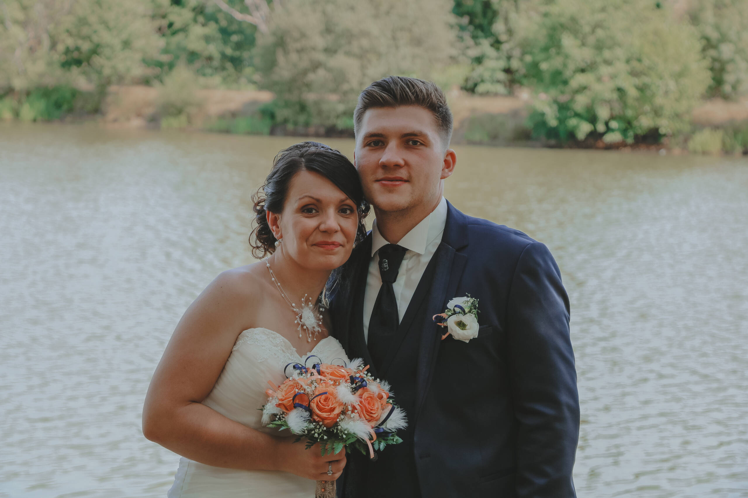 Couple de mariés souriant devant un lac, lors des photos de couple pendant leur mariage, réalisée par Solène photographe.