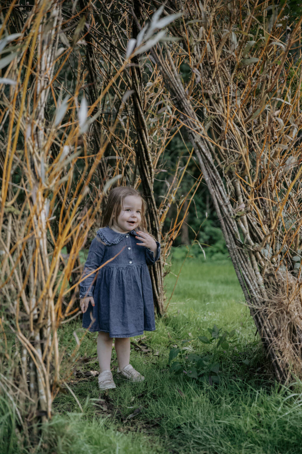 Enfant étonnée et souriante sous un tunnel végétal lors d’une séance photo famille à la Maison de la Rivière à Saint-Georges-de-Montaigu en Vendée, réalisée par Solène photographe.