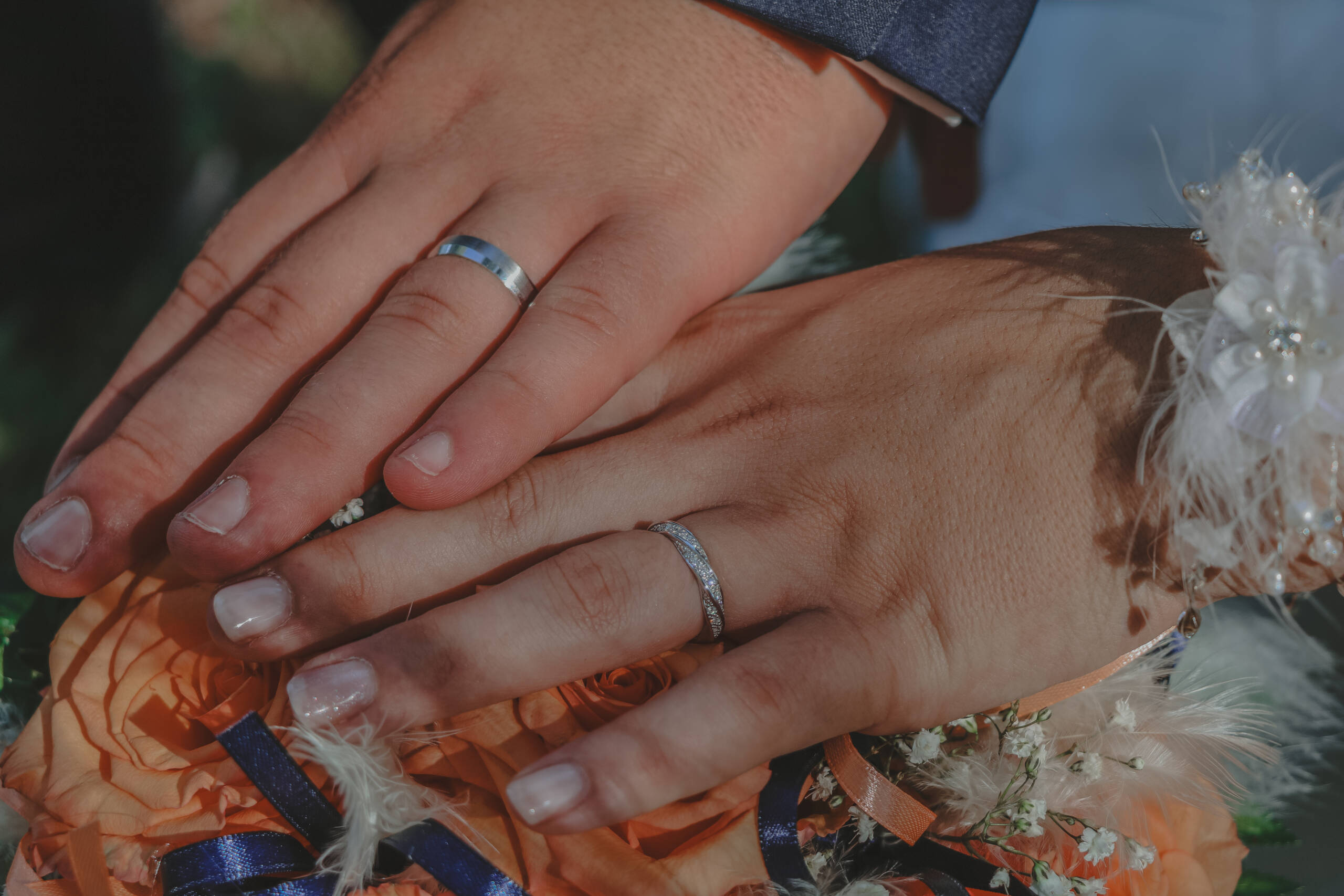 Mains des mariés avec leurs alliances posées sur le bouquet de la mariée, lors des photos de couple pendant leur mariage, réalisée par Solène photographe.