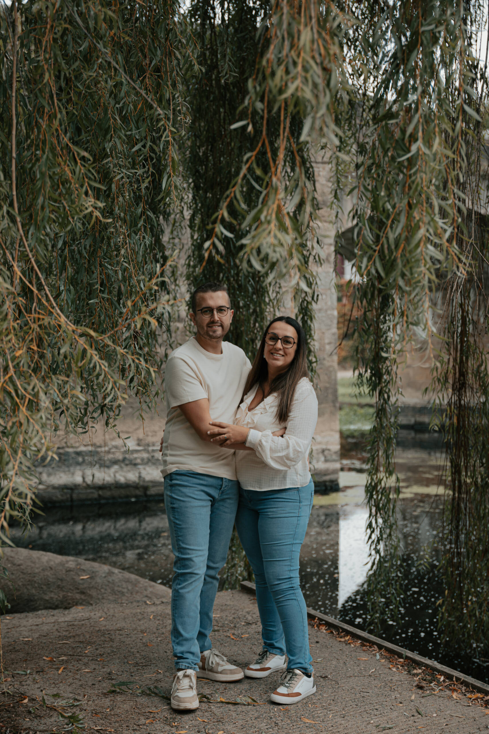 Portrait d'un couple s'enlaçant sous un saule pleureur, lors d’une séance photo engagement à Clisson en Loire-Atlantique, réalisée par Solène photographe.