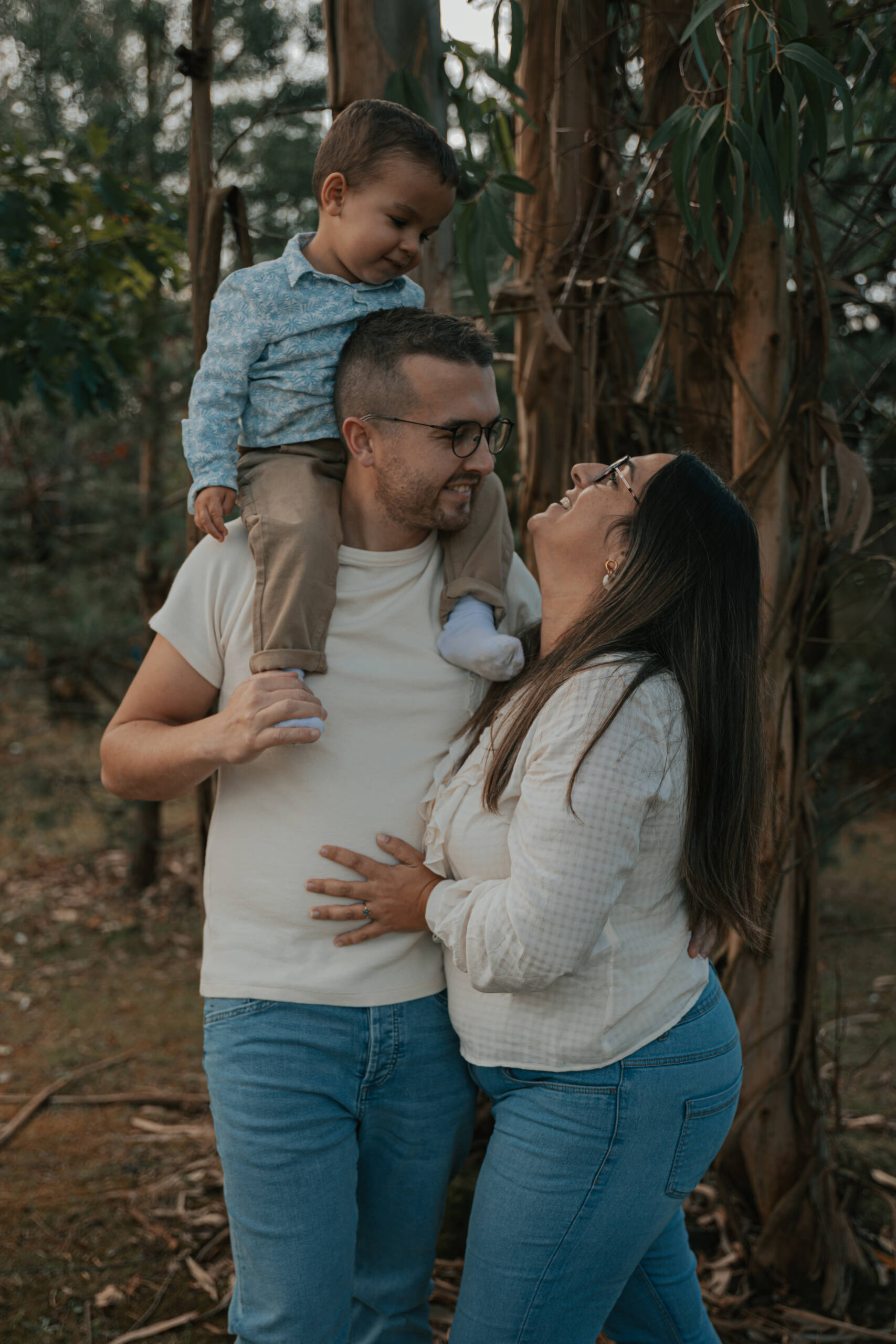 Regard complice d'un couple et de leur fils, monté sur les épaules de son père, lors d’une séance photo engagement en Loire-Atlantique, réalisée par Solène photographe.