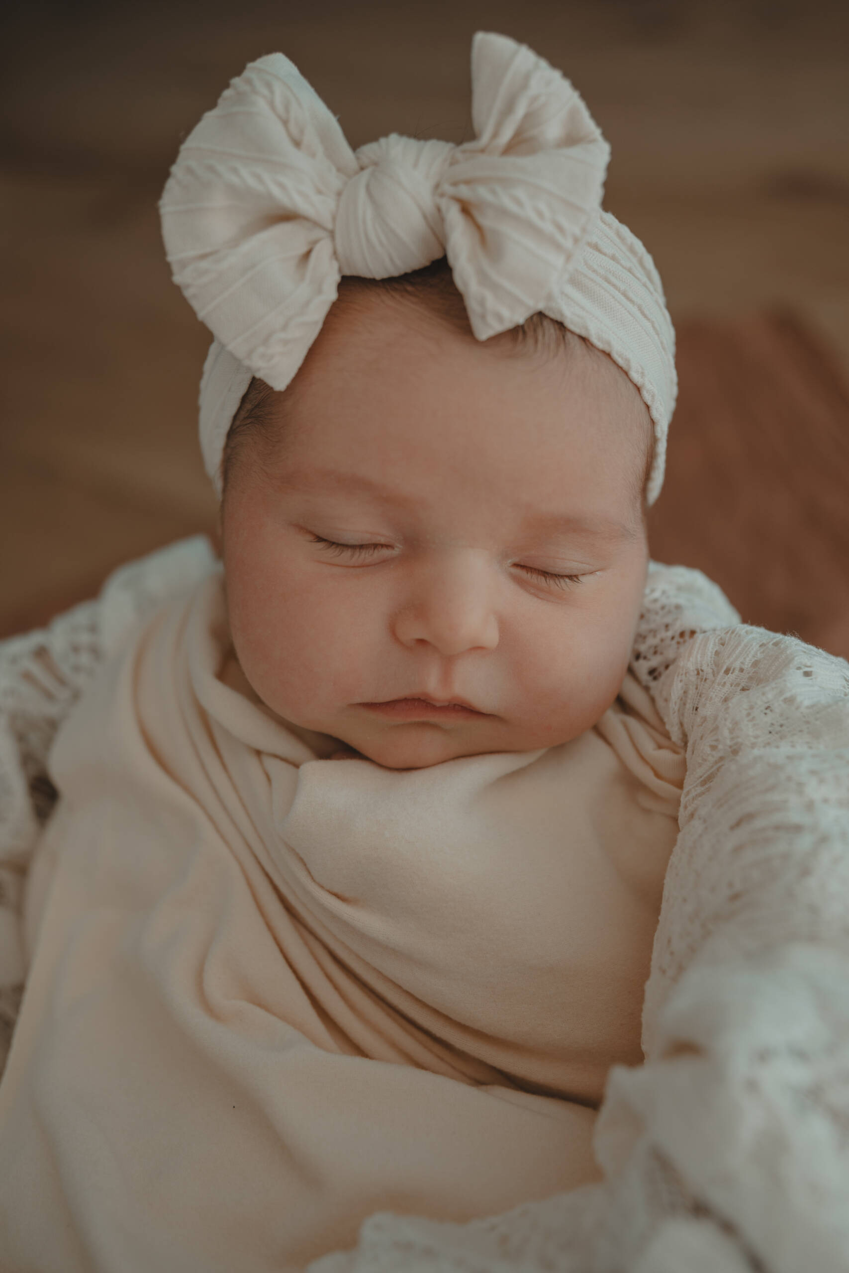 Nourrisson dans un panier avec un nœud sur la tête et enveloppé dans un tissu, lors d’une séance photo naissance à domicile à La Ferrière en Vendée, réalisée par Solène photographe.