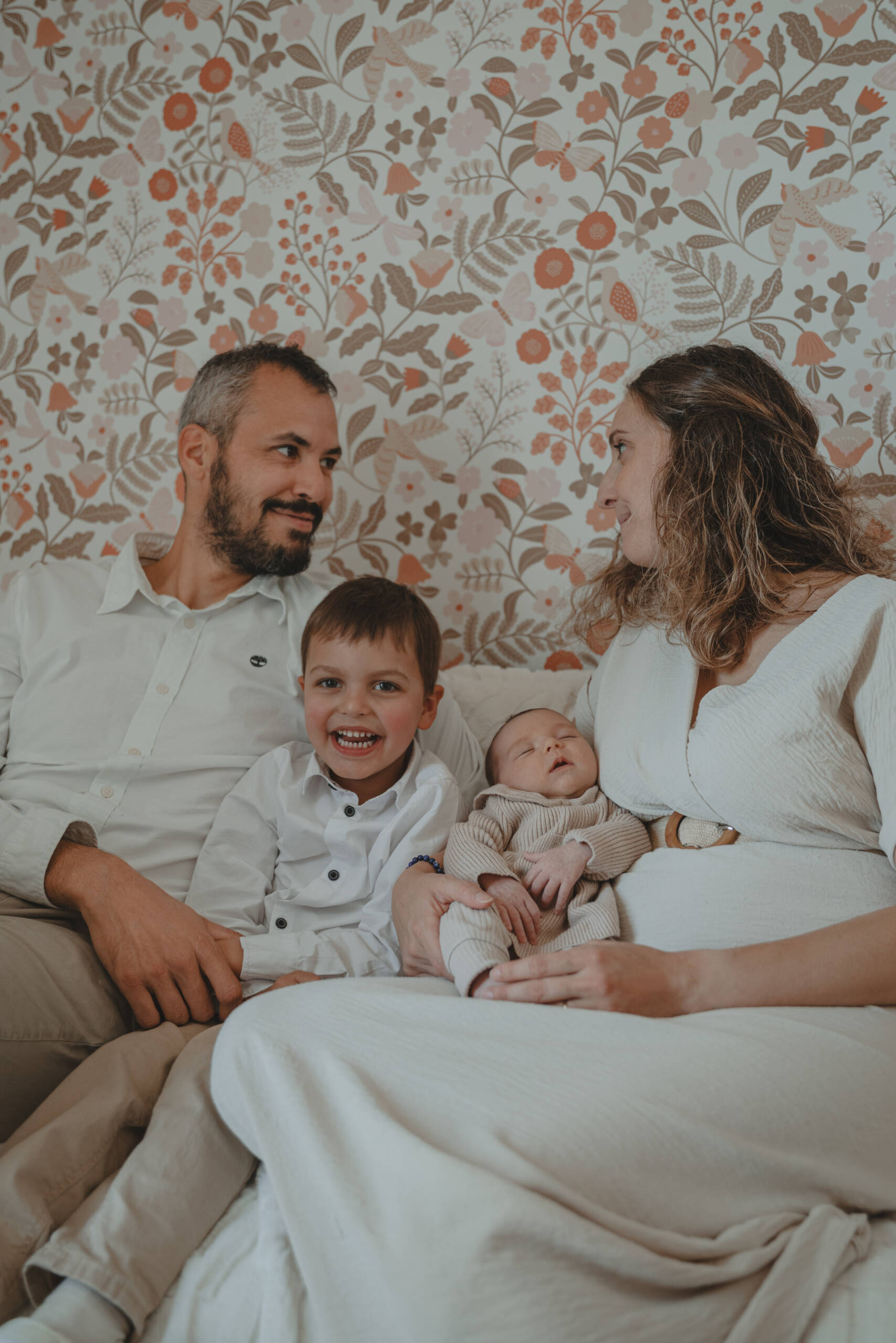 Parents assis sur un canapé se regardant les yeux dans les yeux avec leurs enfants entre eux, lors d’une séance photo naissance à domicile à La Ferrière en Vendée, réalisée par Solène photographe.