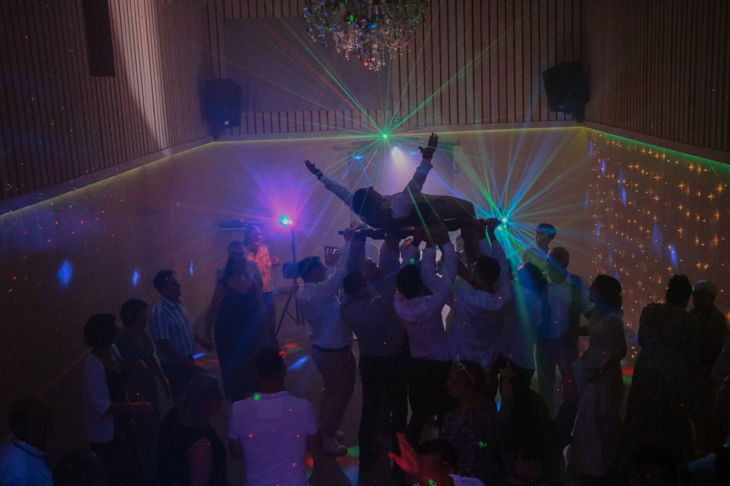 Marié soulevé sur une civière en bois par les invités pendant le bal de son mariage, réalisée par Solène photographe.