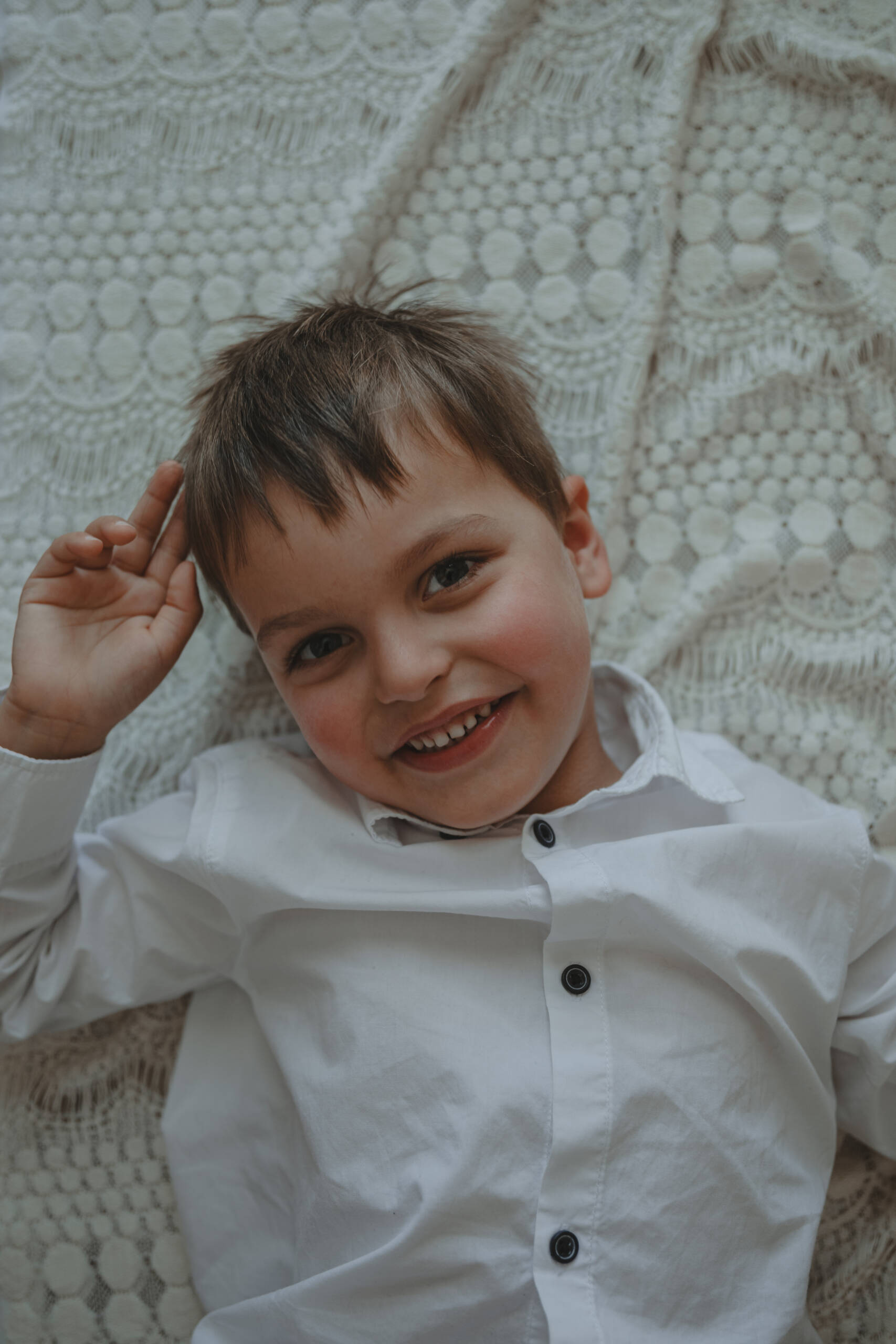 Petit garçon souriant allongé sur une couverture en dentelle lors d’une séance photo naissance à domicile à La Ferrière en Vendée, réalisée par Solène photographe.