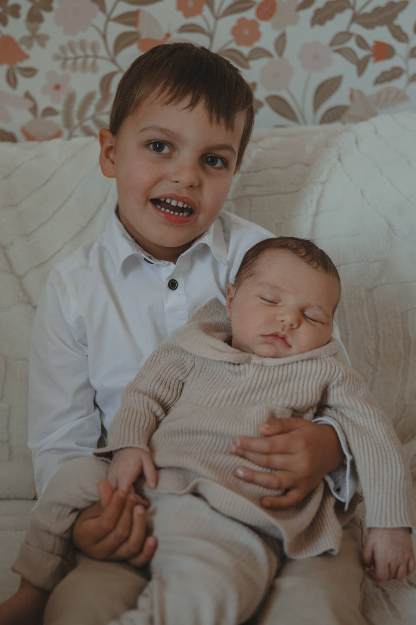 Enfant assis tenant sa petite sœur sur ses genoux, lors d’une séance photo naissance à domicile à La Ferrière en Vendée, réalisée par Solène photographe.