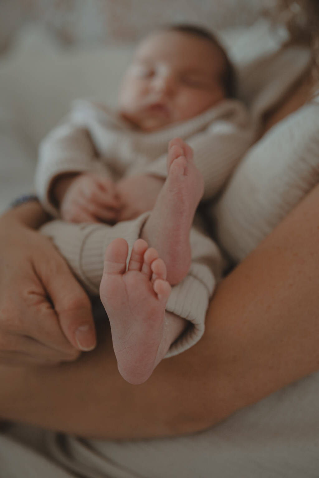 Zoom sur les pieds d'un nourrisson laissant apparaître sa silhouette en arrière plan, lors d’une séance photo naissance à domicile à La Ferrière en Vendée, réalisée par Solène photographe.