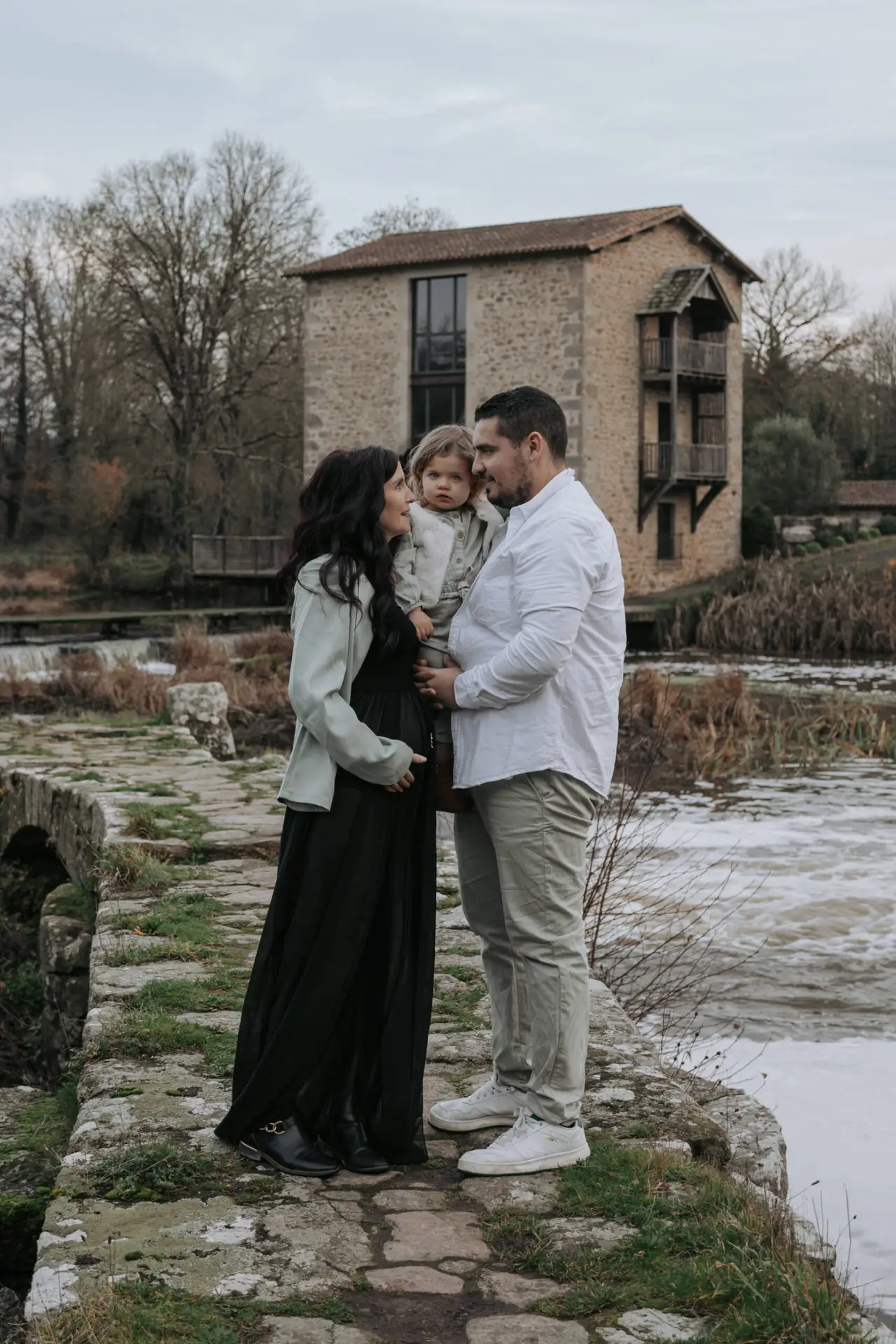 Parents se regardant dans les yeux en tenant leur fille dans les bras, lors d’une séance photo grossesse à Tiffauges en Vendée, réalisée par Solène photographe.