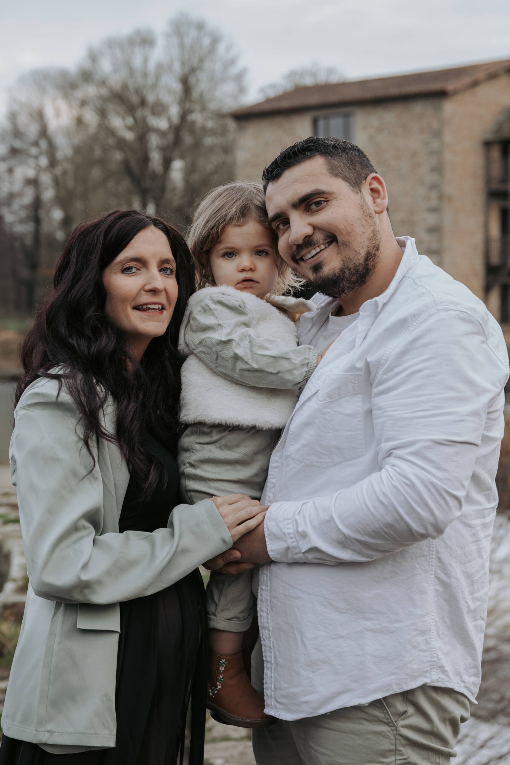 Gros plan sur des parents enlaçant leur petite fille, lors d’une séance photo grossesse à Tiffauges en Vendée, réalisée par Solène photographe.
