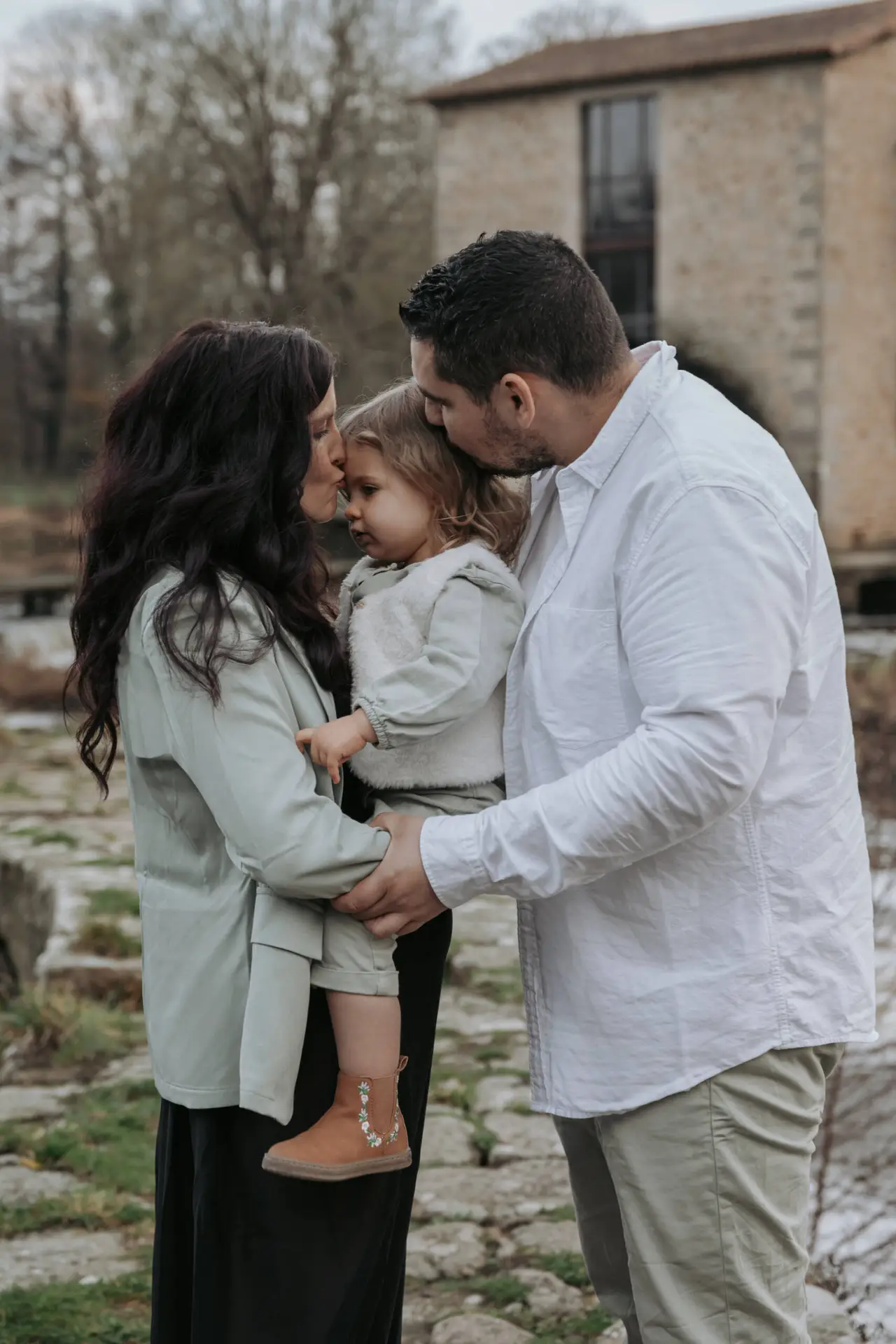 Parents embrassant leur petite fille tenue dans les bras de sa mère lors d’une séance photo grossesse à Tiffauges en Vendée, réalisée par Solène photographe.