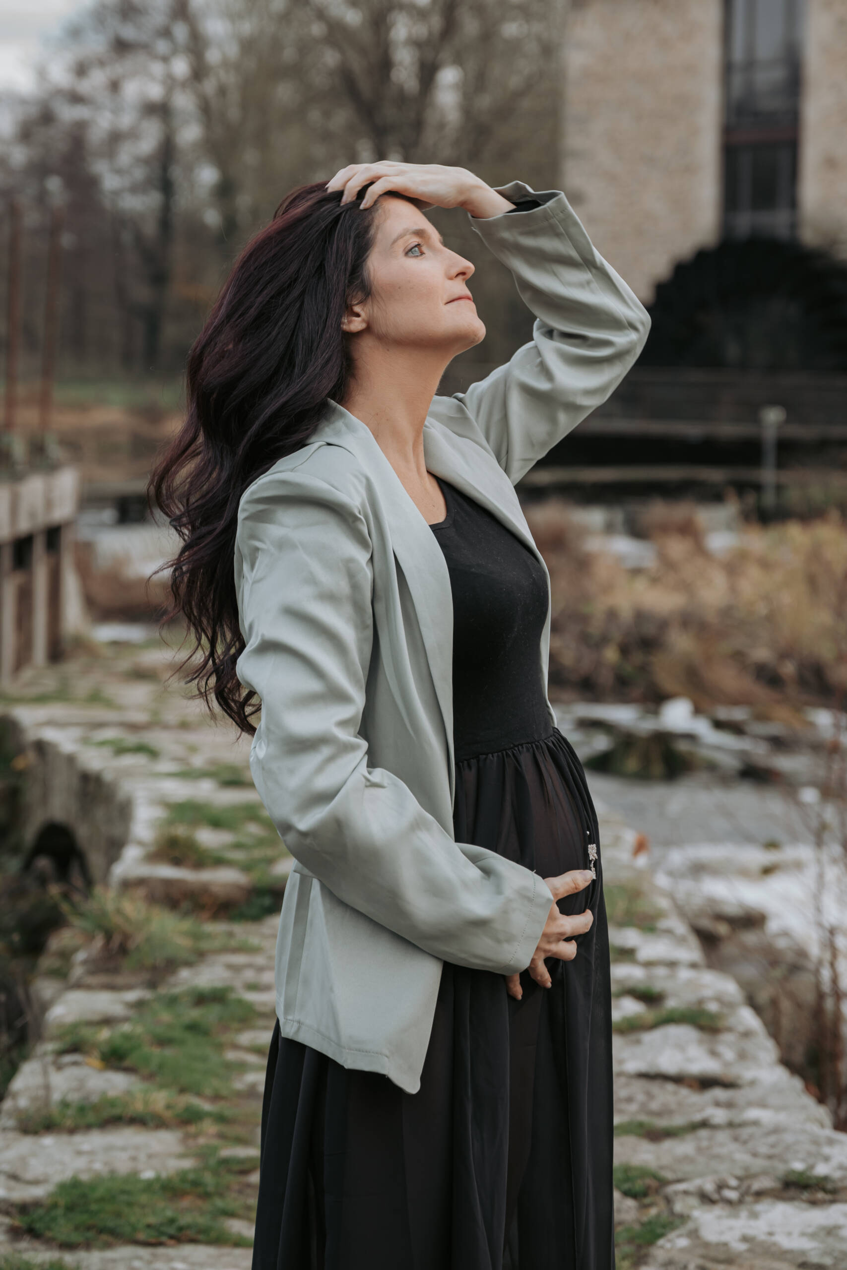 Femme enceinte de profil, debout sur une digue, se tenant les cheveux lors d’une séance photo grossesse à Tiffauges en Vendée, réalisée par Solène photographe.