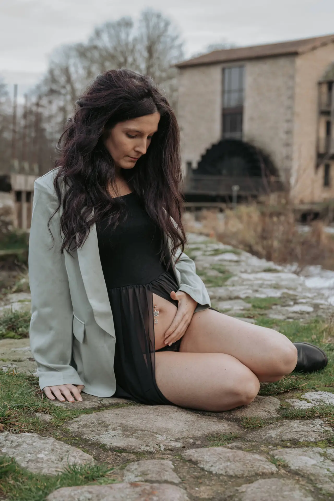 Femme enceinte légèrement de profil, assise sur une digue, se tenant le ventre lors d’une séance photo grossesse à Tiffauges en Vendée, réalisée par Solène photographe.