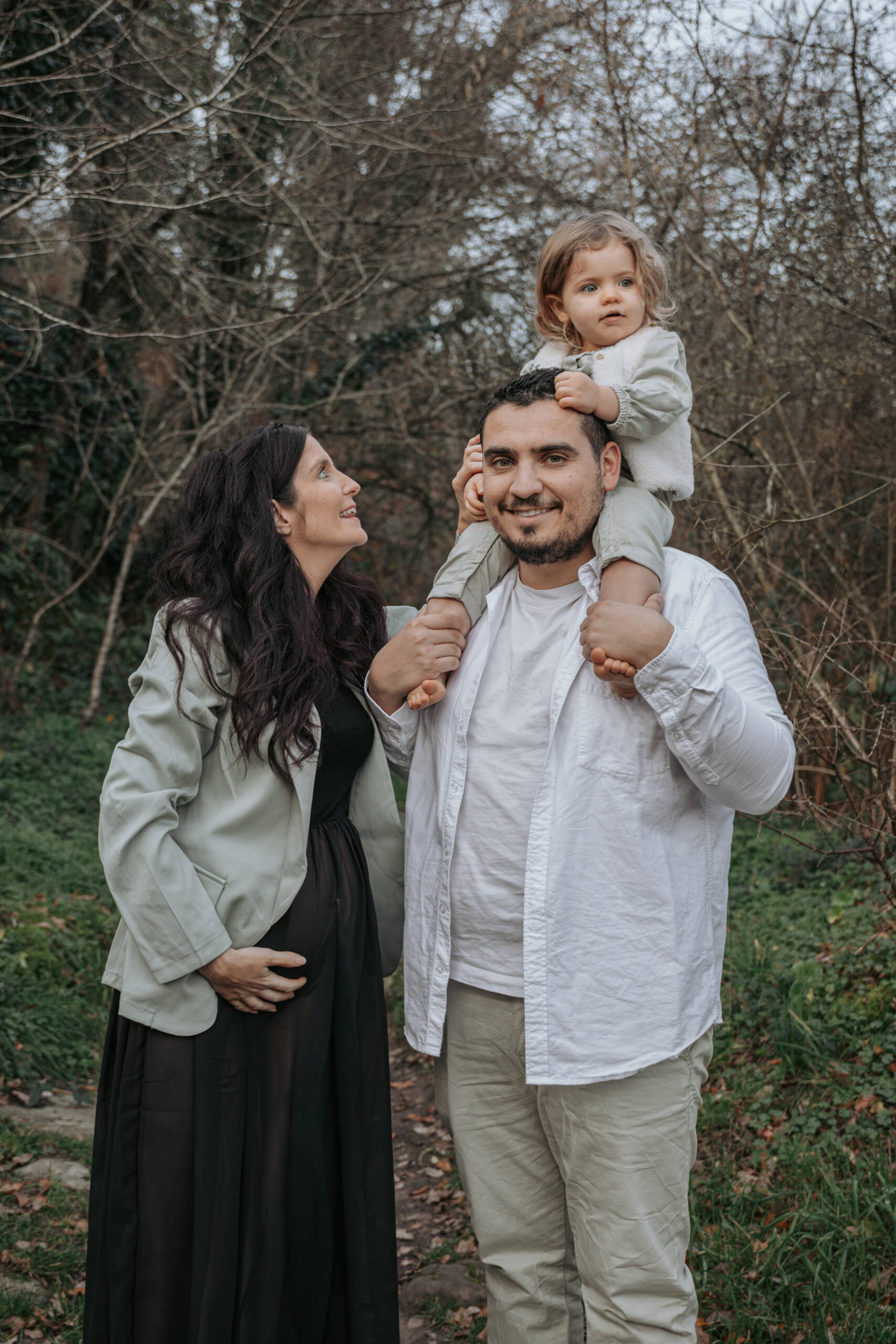 Femme enceinte regardant vers sa fille montée sur les épaules de son père, lors d’une séance photo grossesse à Tiffauges en Vendée, réalisée par Solène photographe.