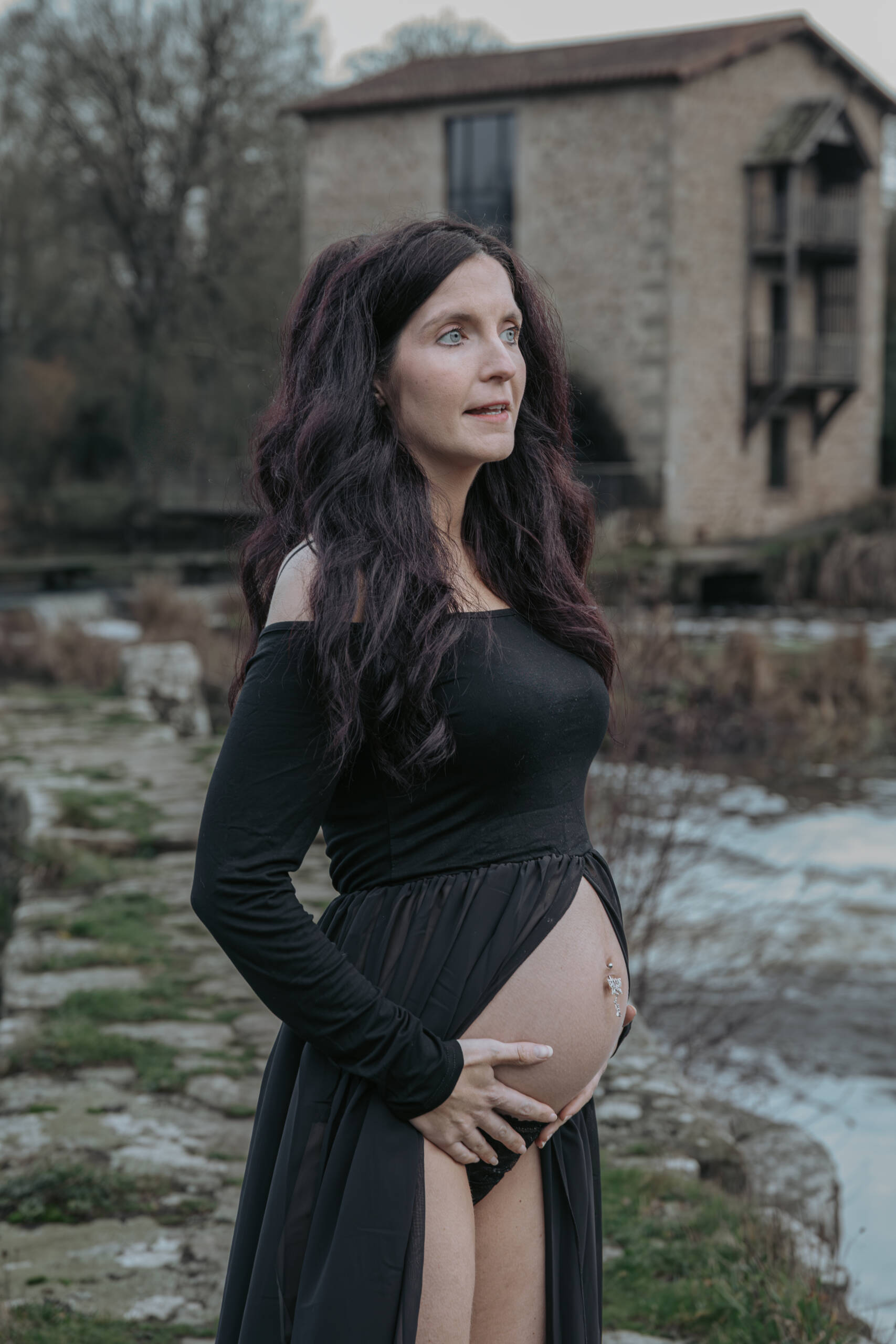 Femme enceinte légèrement de profil, debout sur une digue, se tenant le ventre lors d’une séance photo grossesse à Tiffauges en Vendée, réalisée par Solène photographe.