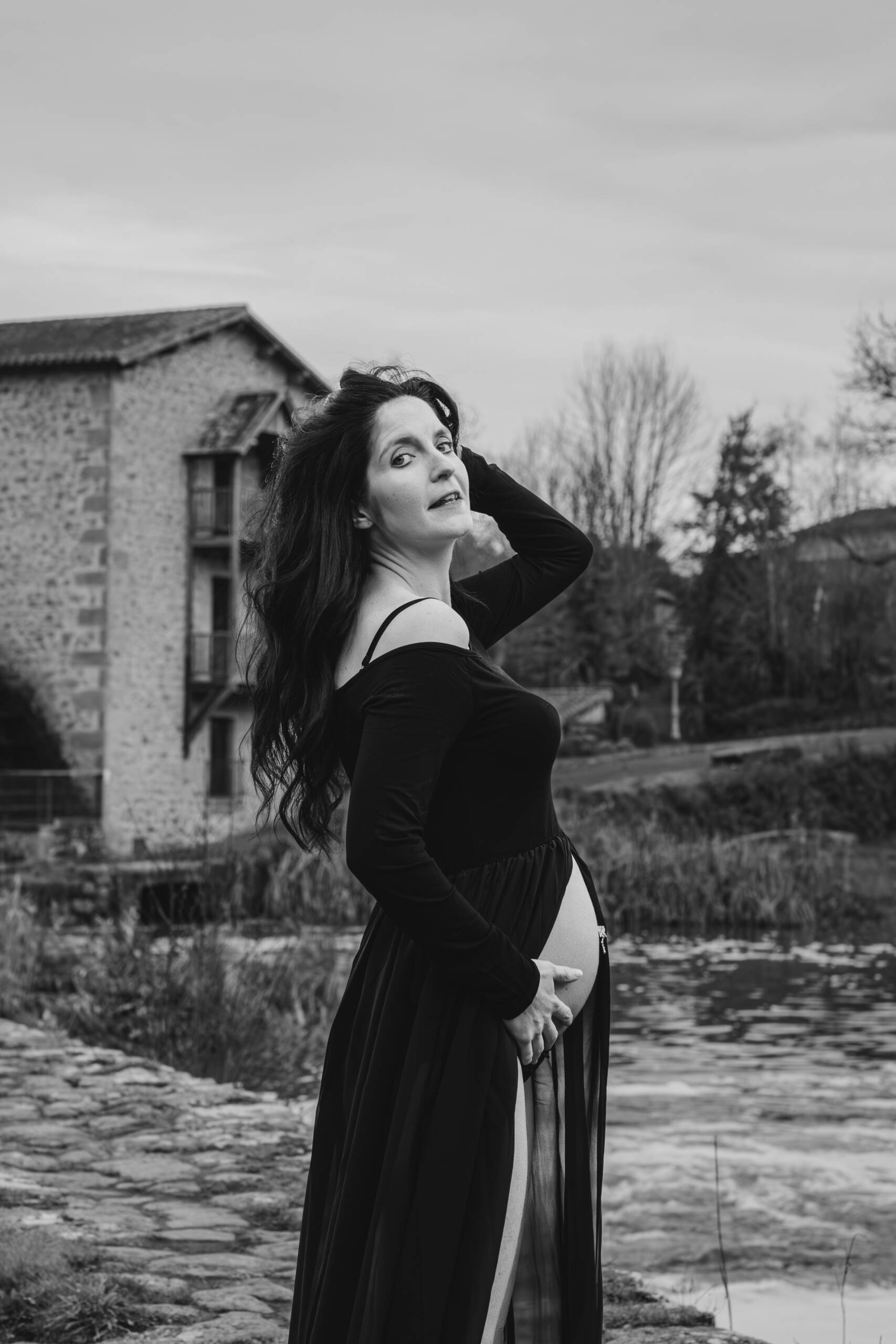 Femme enceinte de profil, debout sur une digue, se tenant les cheveux lors d’une séance photo grossesse à Tiffauges en Vendée, réalisée en noir et blanc par Solène photographe.