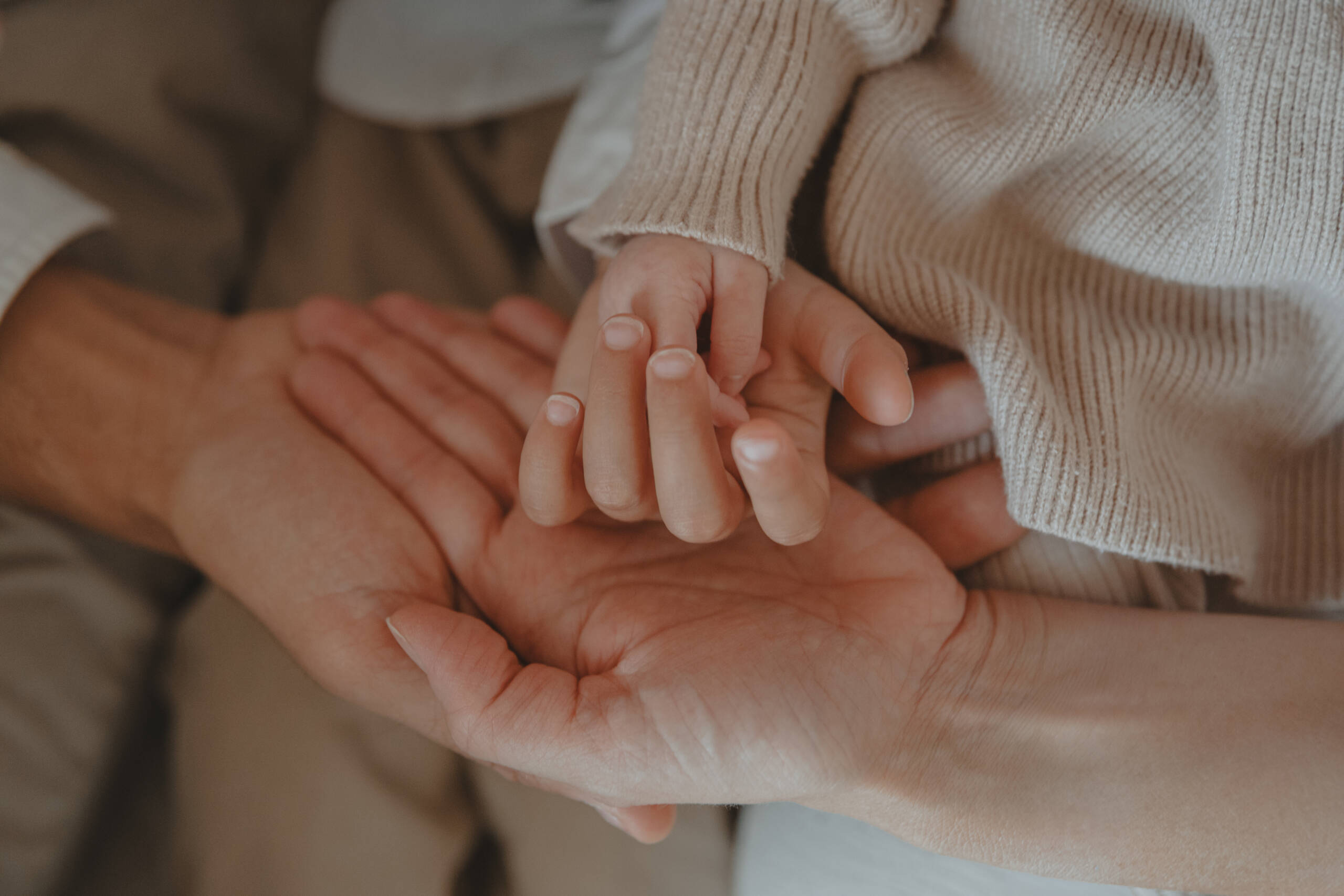Superposition des mains de toute une famille, nourrisson, enfant et leur deux parents, lors d’une séance photo naissance à domicile à La Ferrière en Vendée, réalisée par Solène photographe.