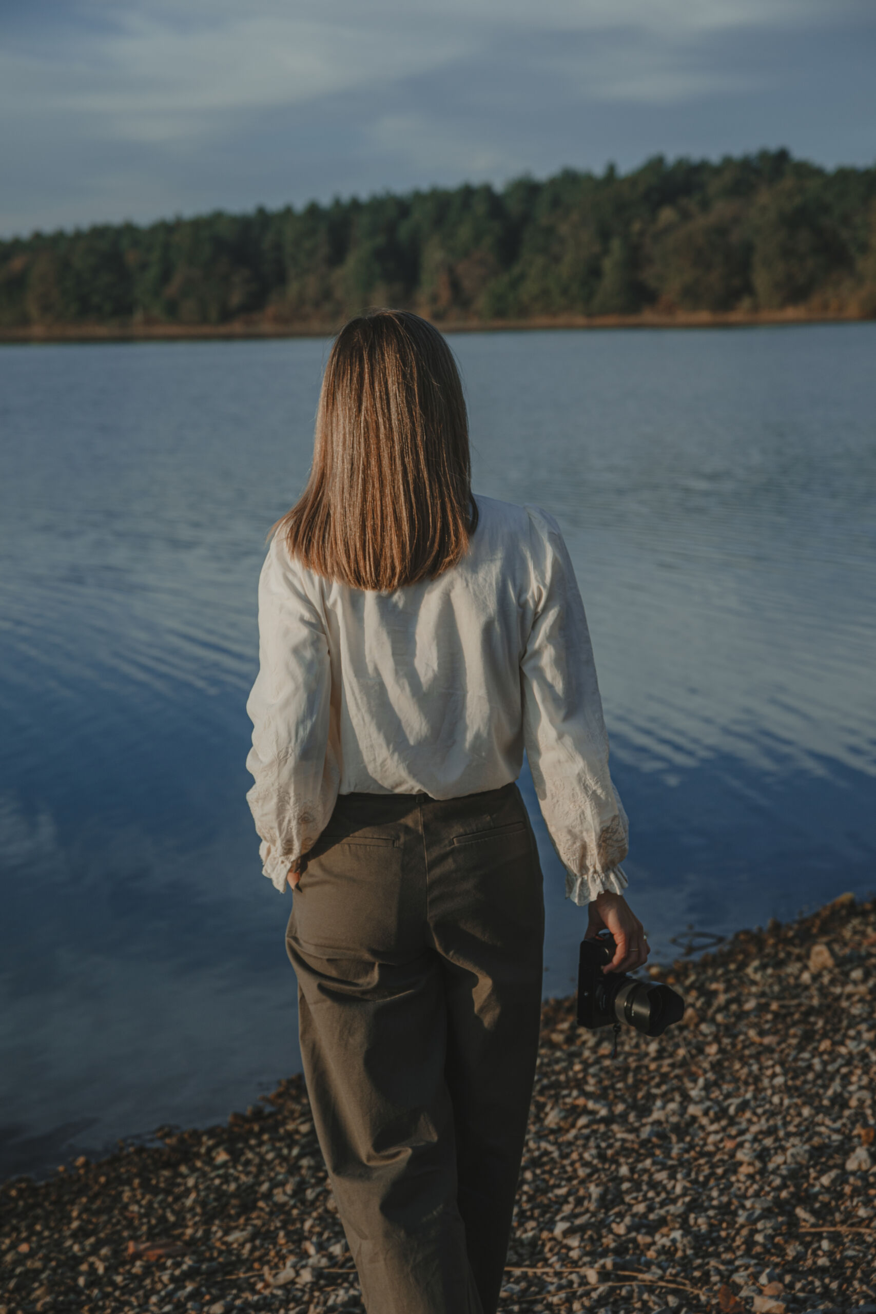 Femme marchant vers un lac, appareil photo à la main, lors d’une séance portrait professionnel à La Roche-sur-Yon en Vendée, réalisée par Solène photographe.