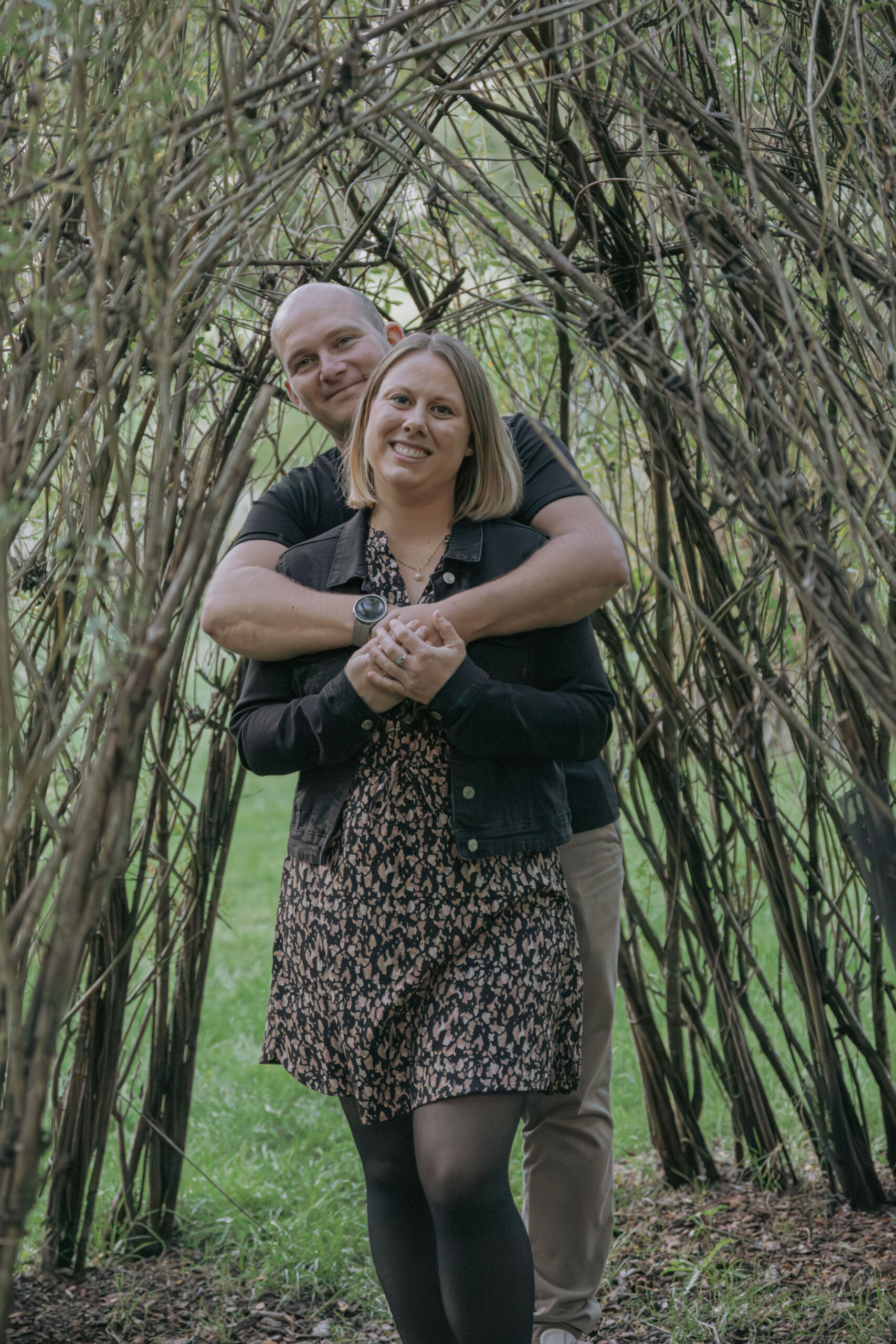 Couple s'enlaçant sous une arche végétale lors d’une séance photo famille à la Maison de la Rivière à Saint-Georges-de-Montaigu en Vendée, réalisée par Solène photographe.