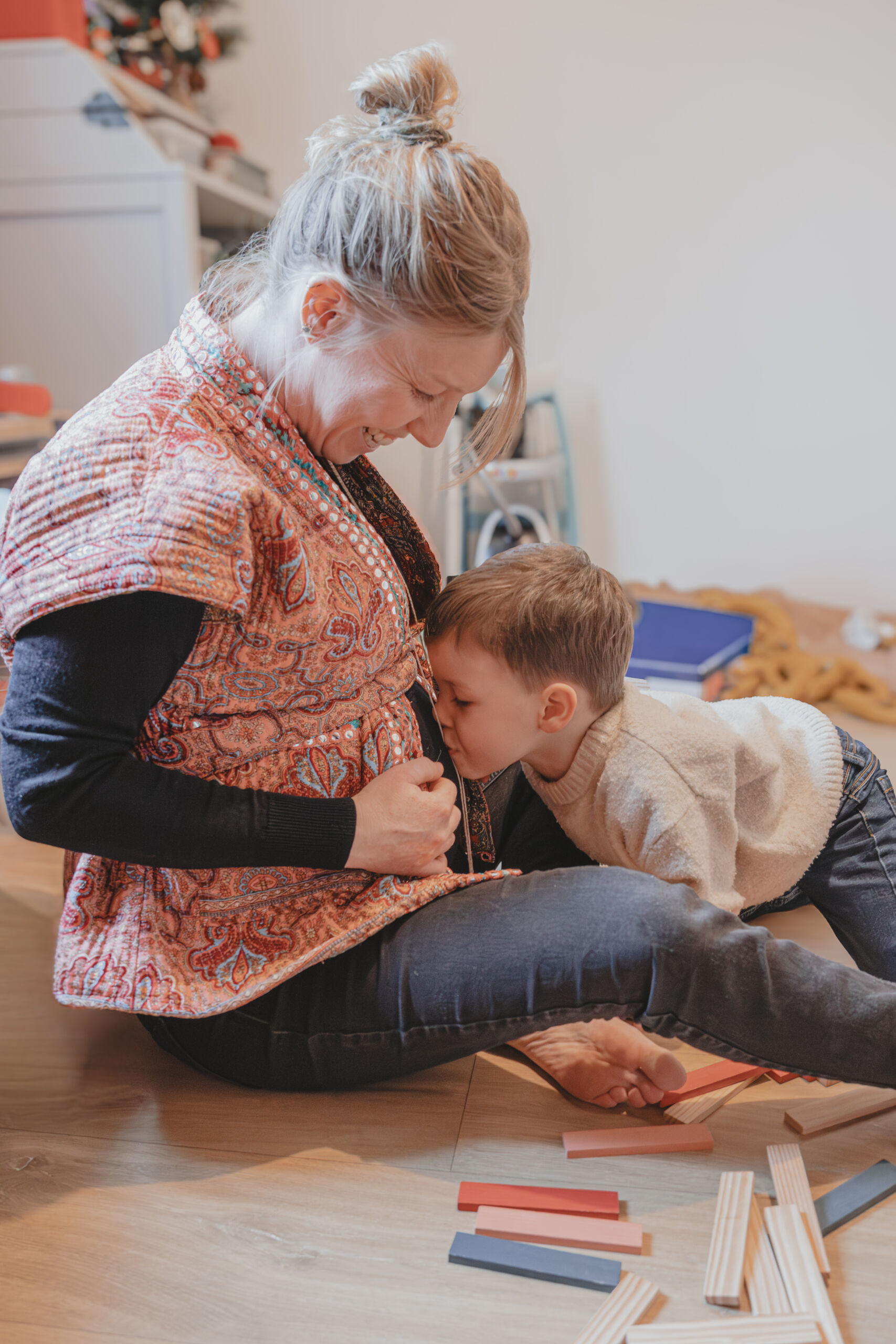 Enfant faisant un bisou sur le ventre rond de sa mère pendant une partie de kapla, lors d’une séance photo grossesse à Dompierre-sur-Yon en Vendée, réalisée par Solène photographe.