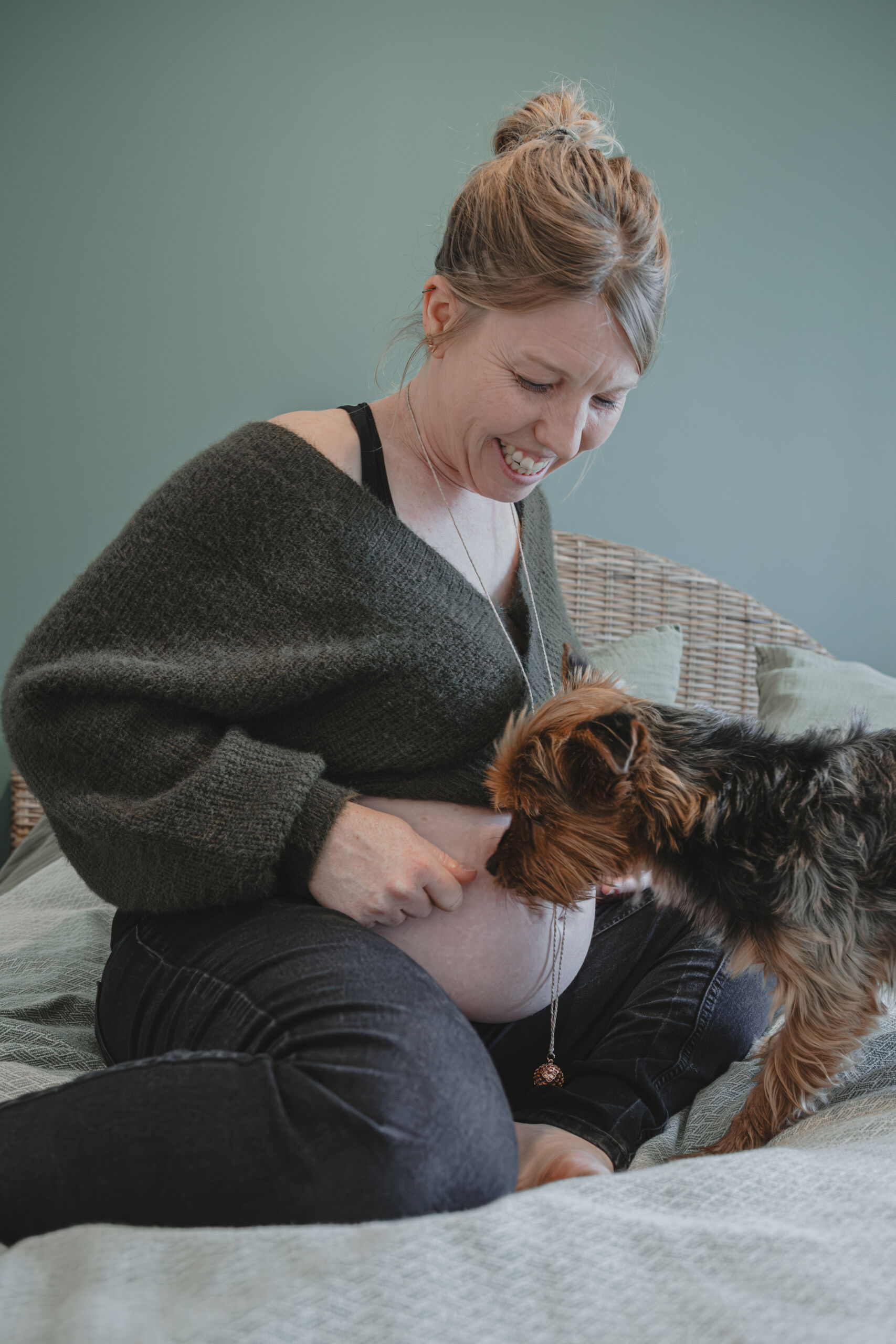 Femme enceinte souriante sur un lit avec son chien, lors d’une séance photo grossesse à Dompierre-sur-Yon en Vendée, réalisée par Solène photographe.