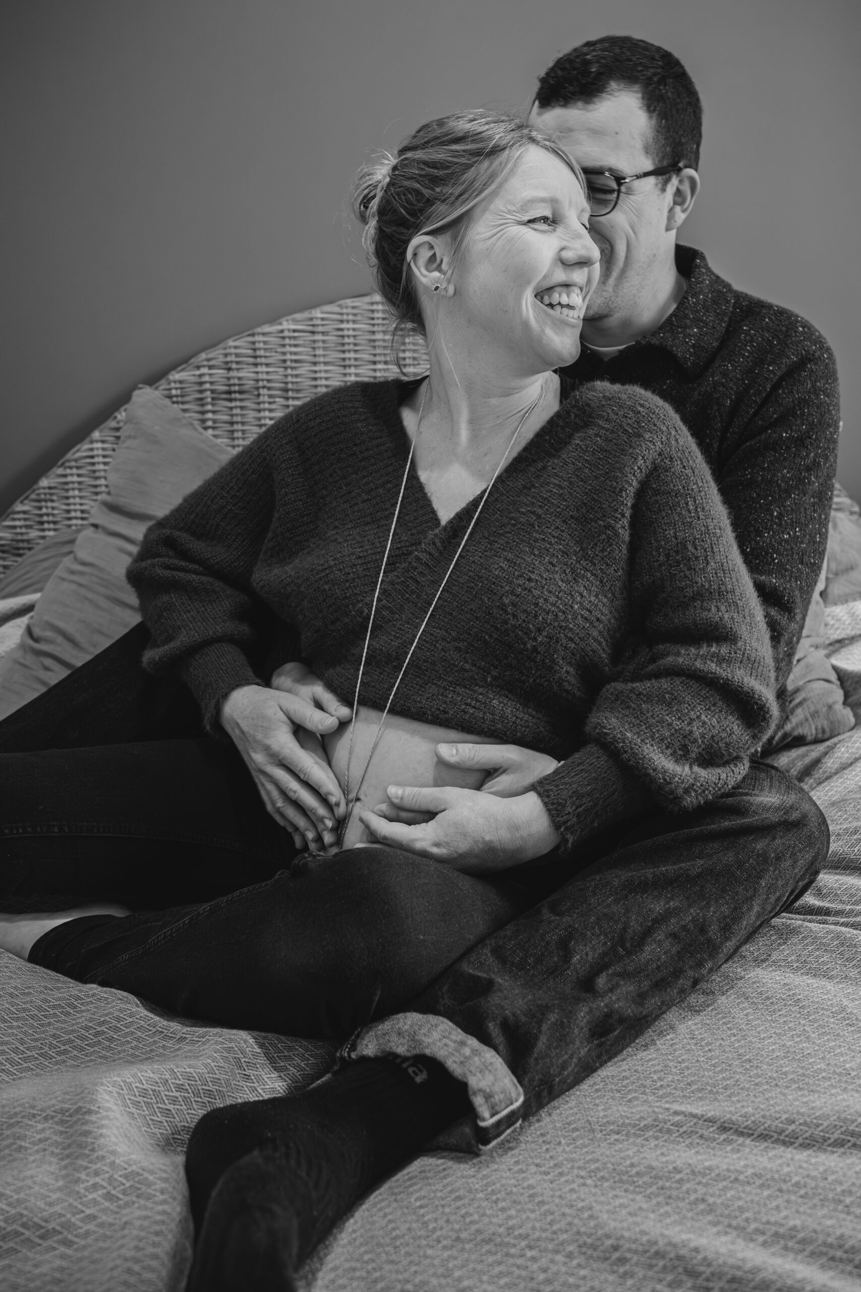 Futurs parents complices et heureux rejoignant leurs mains sur le ventre rond de la femme, lors d’une séance photo grossesse à Dompierre-sur-Yon en Vendée, réalisée en noir et blanc par Solène photographe.