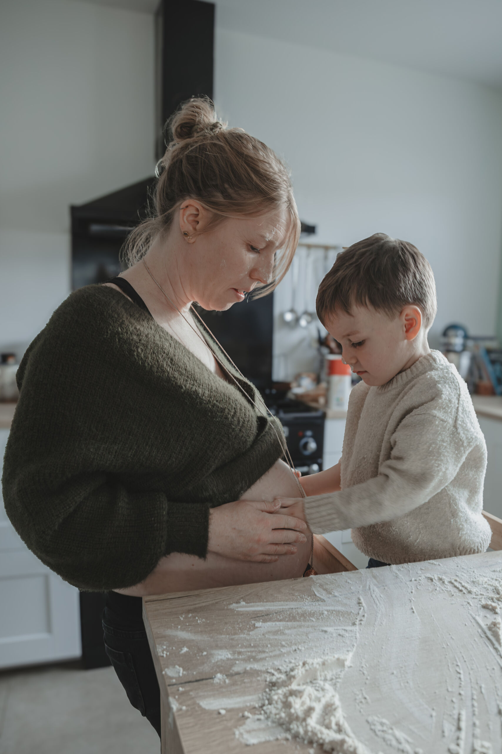 Enfant mettant ses mains remplies de farine sur le ventre rond de sa mère, lors d’une séance photo grossesse à Dompierre-sur-Yon en Vendée, réalisée par Solène photographe.