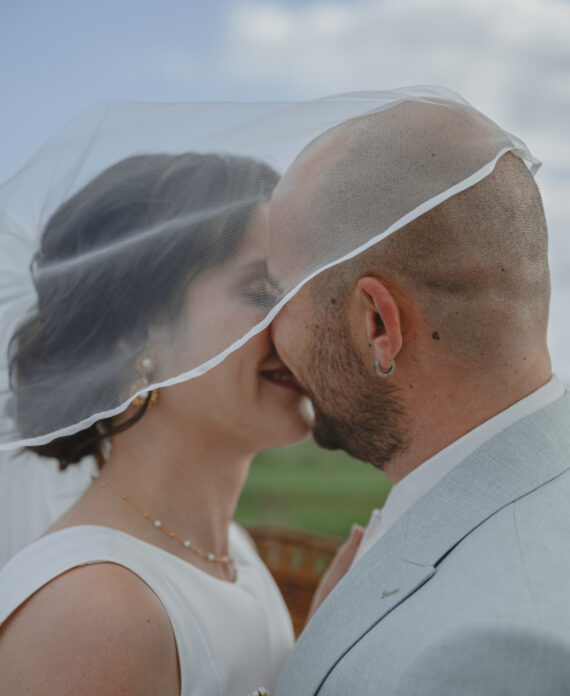 Mariés prêt à s'embrasser sous le voile de la mariée lors d'une cérémonie laïque pendant leur mariage au Domaine Quatre Plumes aux Landes-Génusson en Vendée, réalisée par Solène photographe.