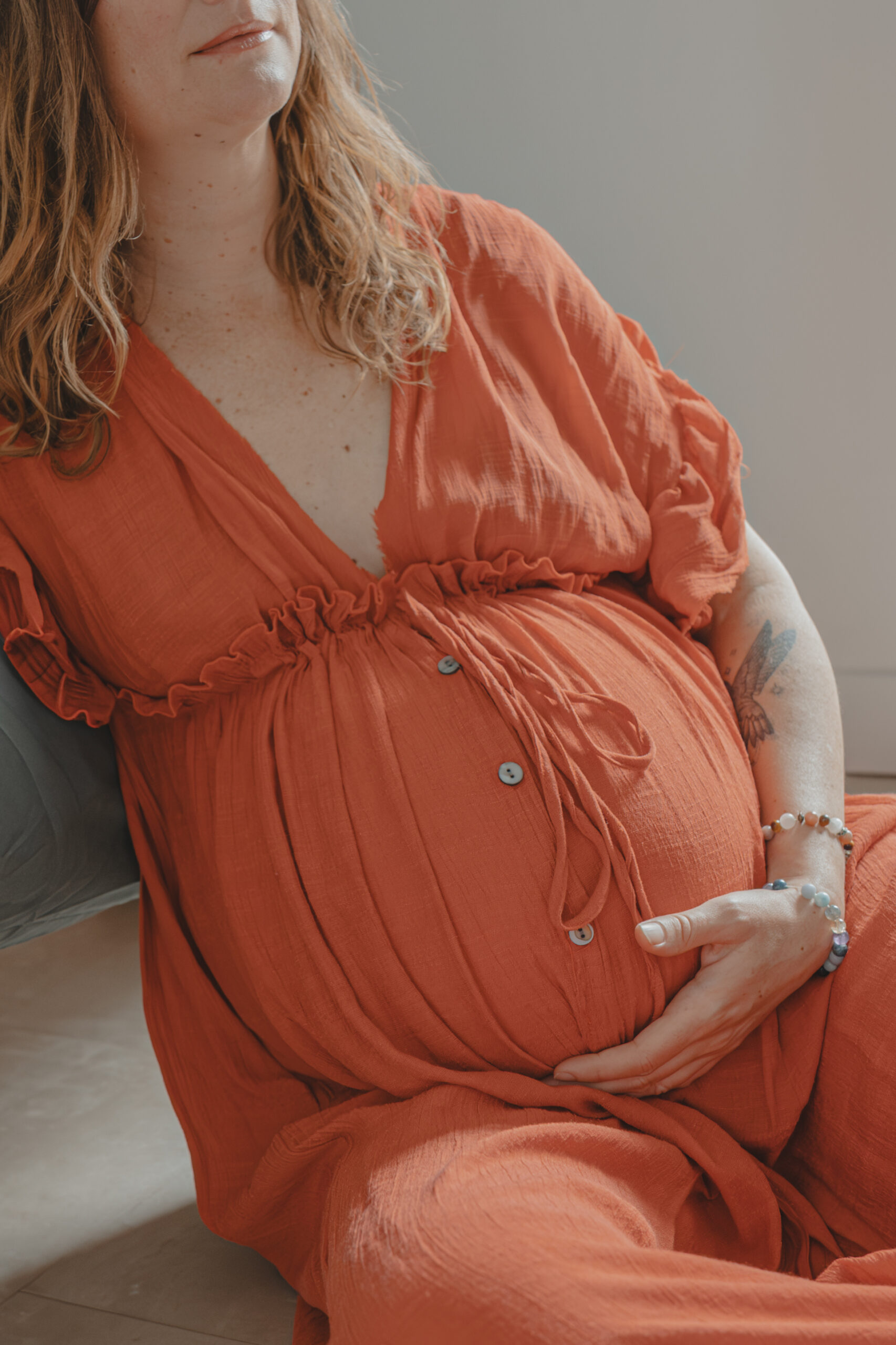 Femme vêtue d'une robe orange avec un ventre arrondi et sa main placée en-dessous, lors d’un shooting confiance en soi à Montbert en Loire- Atlantique, réalisée par Solène photographe.