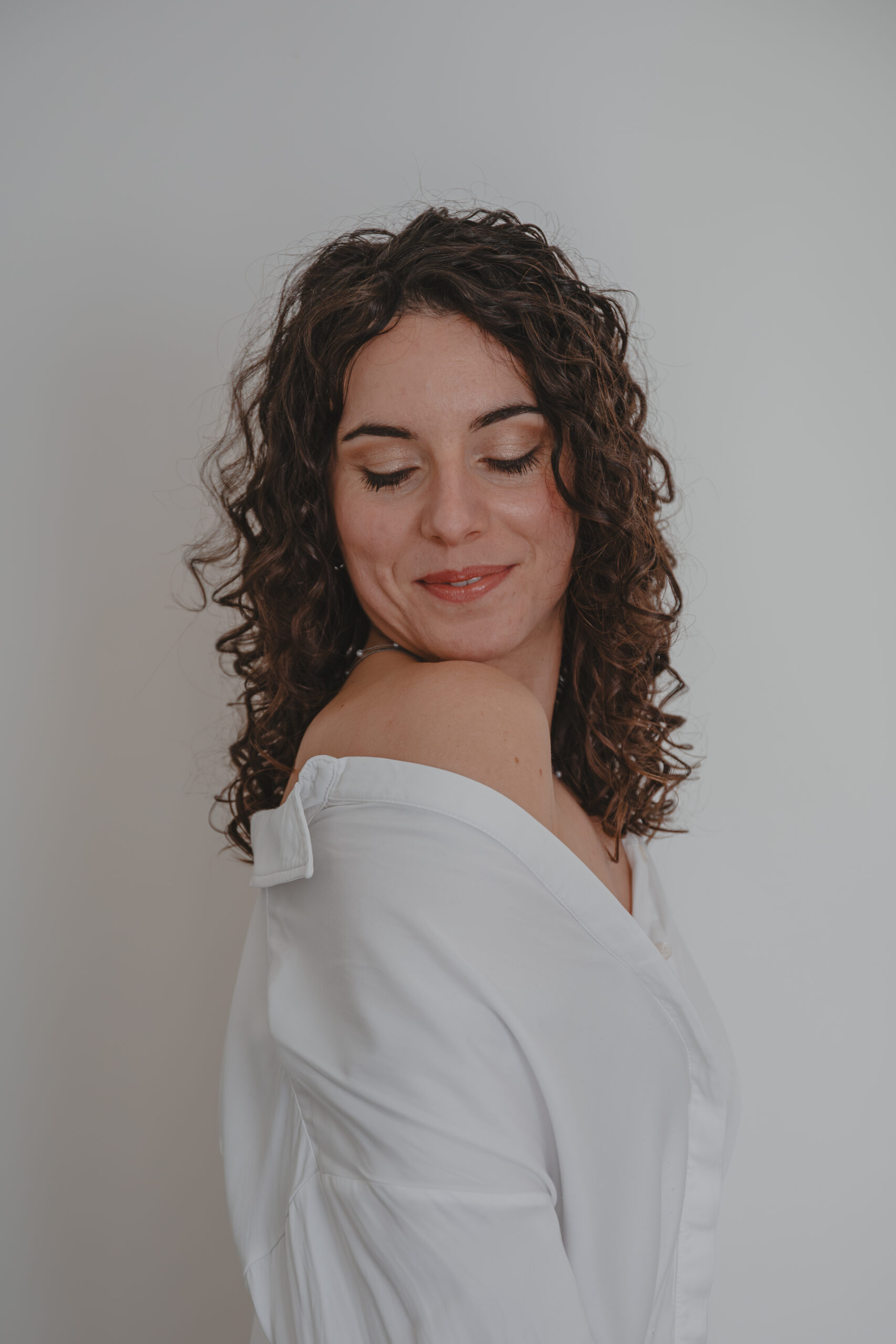 Femme souriante de profil se tenant debout en chemise blanche avec une épaule dénudée, lors d’un shooting confiance en soi à Montbert en Loire- Atlantique, réalisée par Solène photographe.