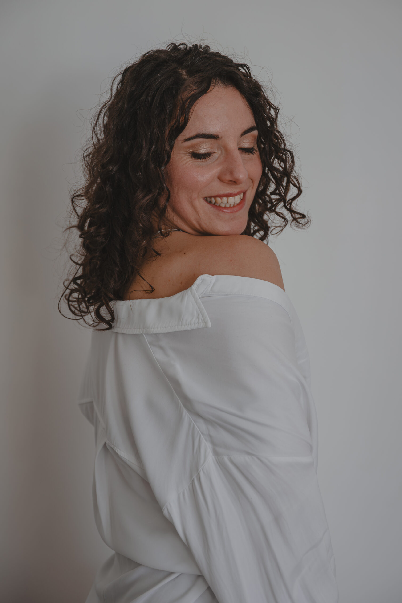 Femme souriante se tenant debout en chemise blanche avec une épaule dénudée, lors d’un shooting confiance en soi à Montbert en Loire- Atlantique, réalisée par Solène photographe.