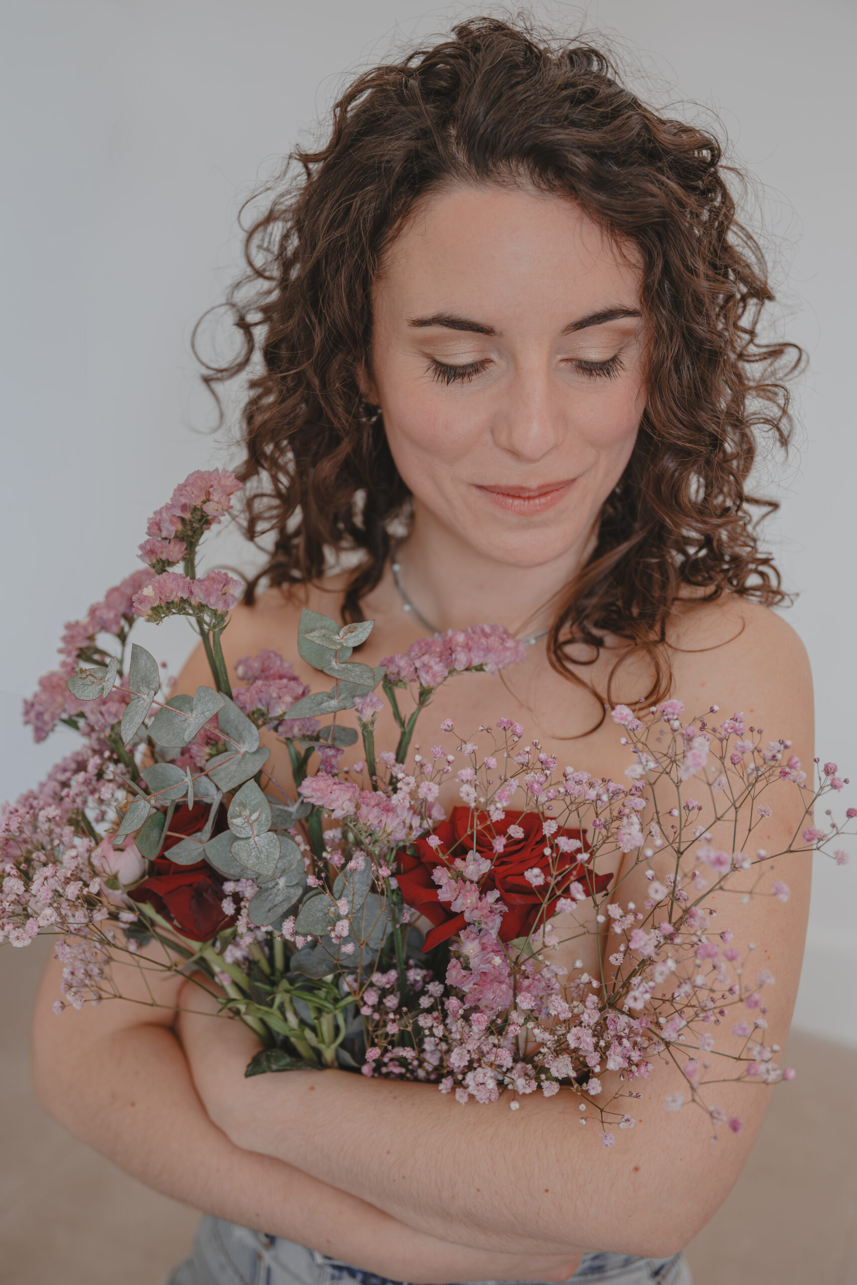 Femme regardant vers le bouquet de fleurs tenue dans ses bras qui cache sa poitrine, lors d’un shooting confiance en soi à Montbert en Loire- Atlantique, réalisée par Solène photographe.