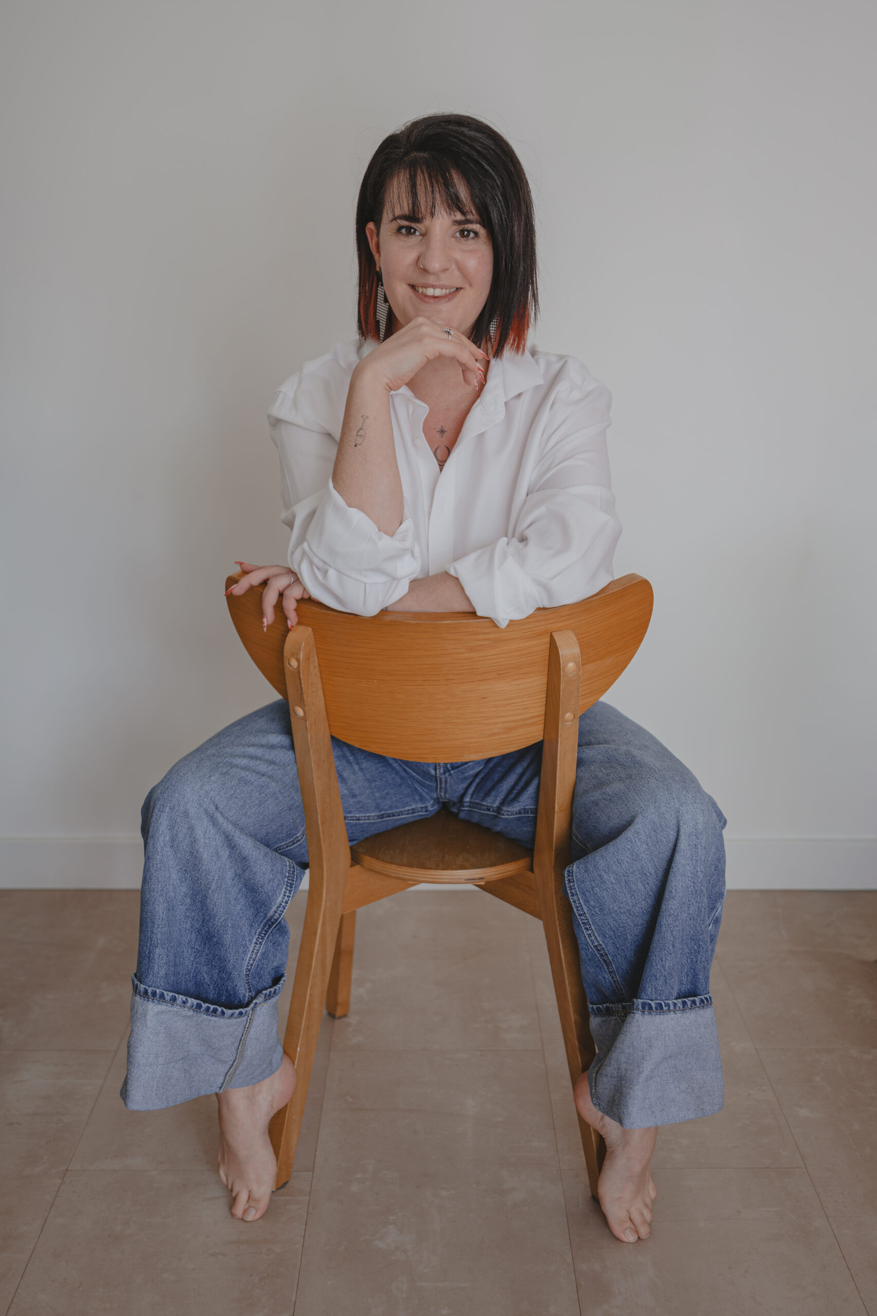 Femme souriante assise à l'envers sur une chaise accoudée au dossier, lors d’un shooting confiance en soi à Montbert en Loire- Atlantique, réalisée par Solène photographe.