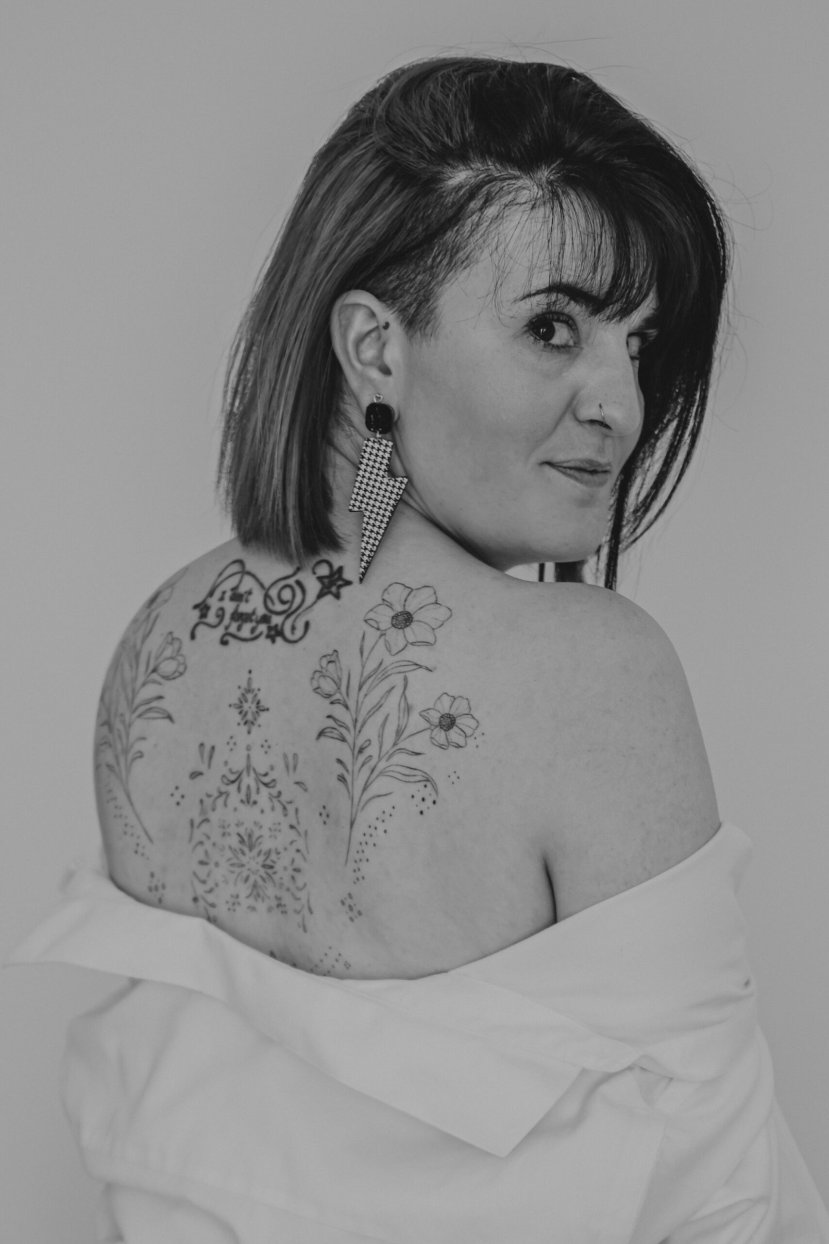 Femme se retournant vers l'objectif épaules dénudées dévoilant des tatouages, lors d’un shooting confiance en soi à Montbert en Loire- Atlantique, réalisée en noir et blanc par Solène photographe.