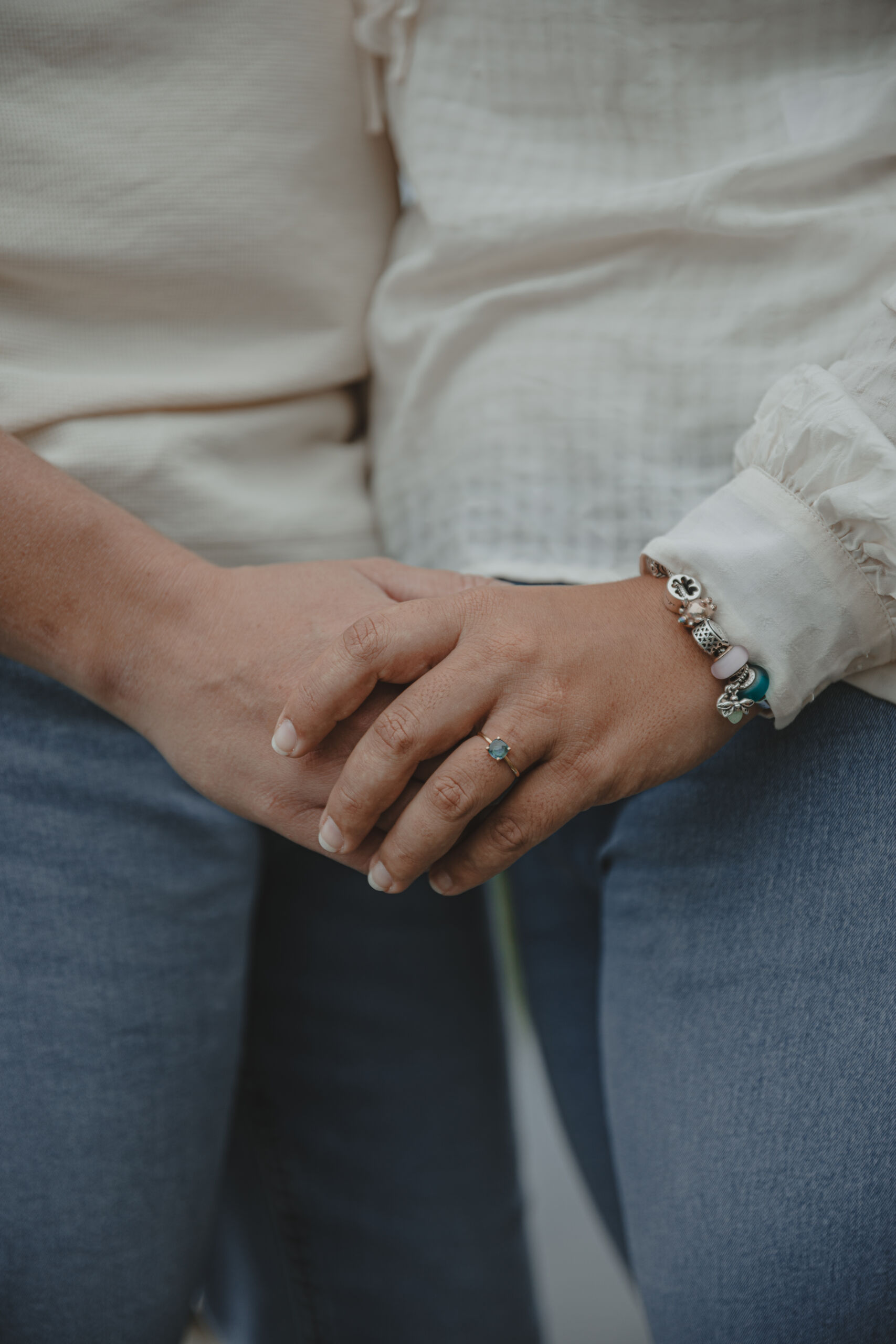 Zoom sur des mains réunies devant un couple enlacé, mettant en valeur la bague de fiançailles à diamant bleu, lors d’une séance photo engagement à Clisson en Loire-Atlantique, réalisée par Solène photographe.