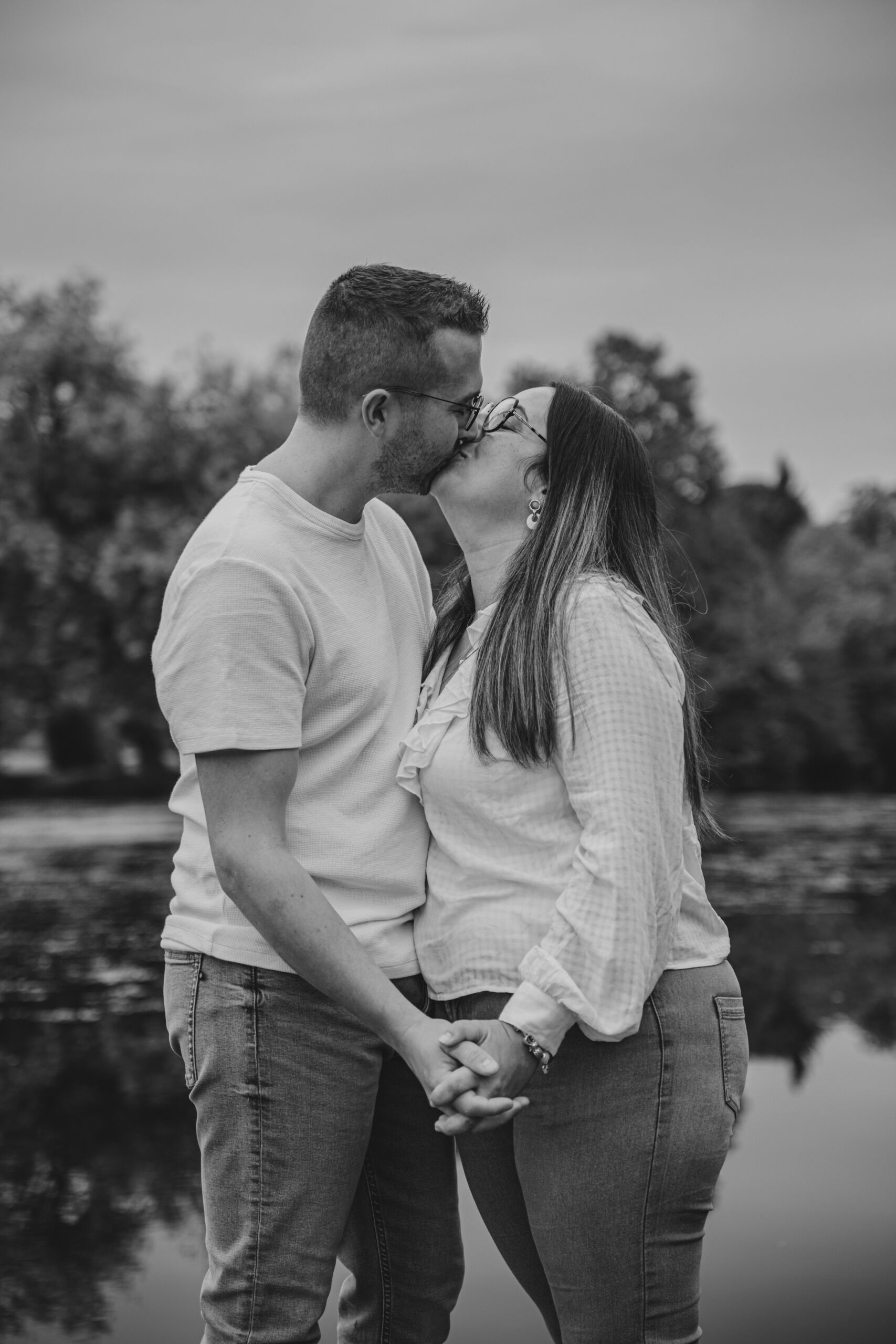 Couple heureux enlacé s'embrassant en se tenant la main, lors d’une séance photo engagement à Clisson en Loire-Atlantique, réalisée en noir et blanc par Solène photographe.