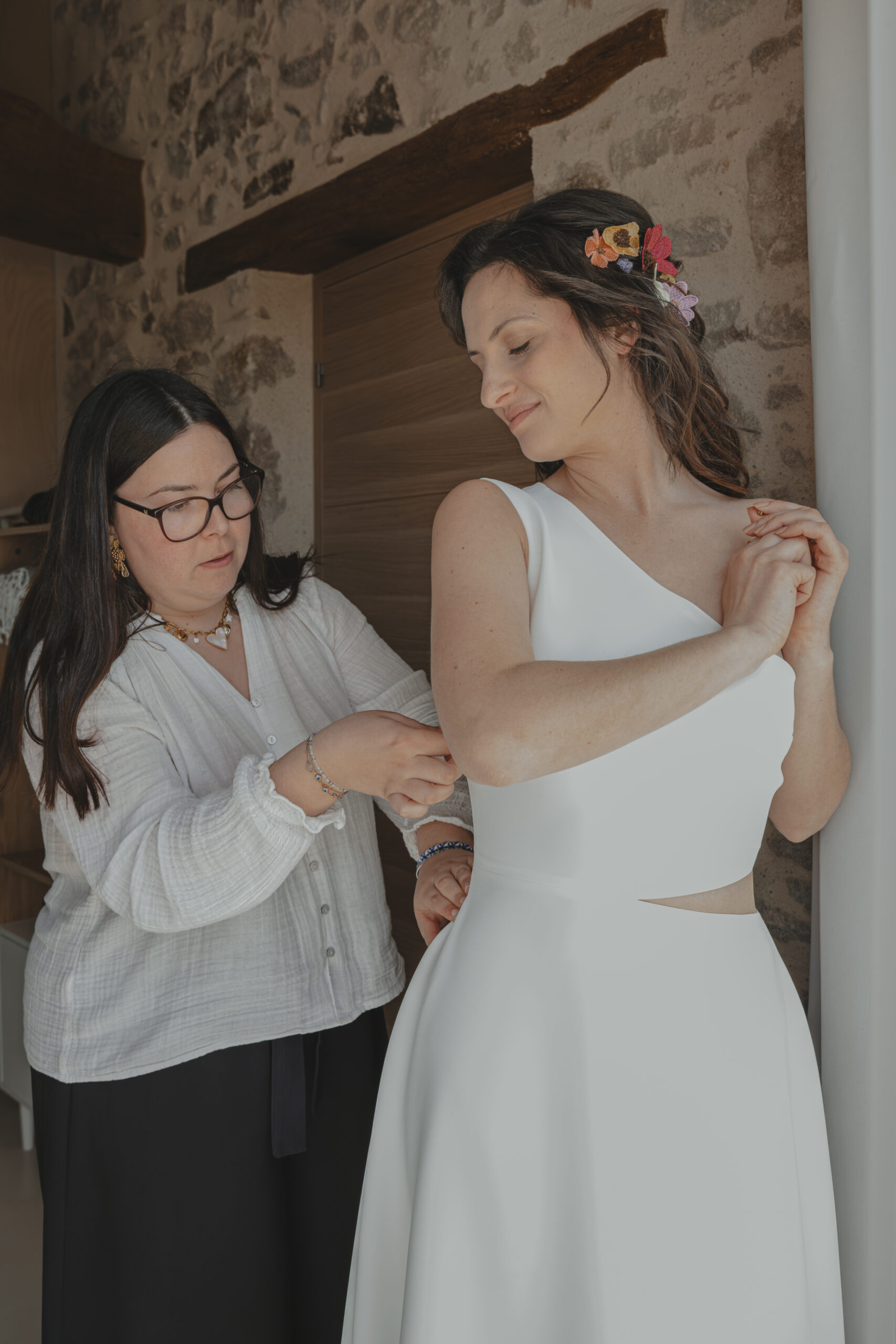 Femme fermant la robe de la mariée pendant les préparatifs de son mariage au Domaine Quatre Plumes aux Landes-Génusson en Vendée, réalisée par Solène photographe.
