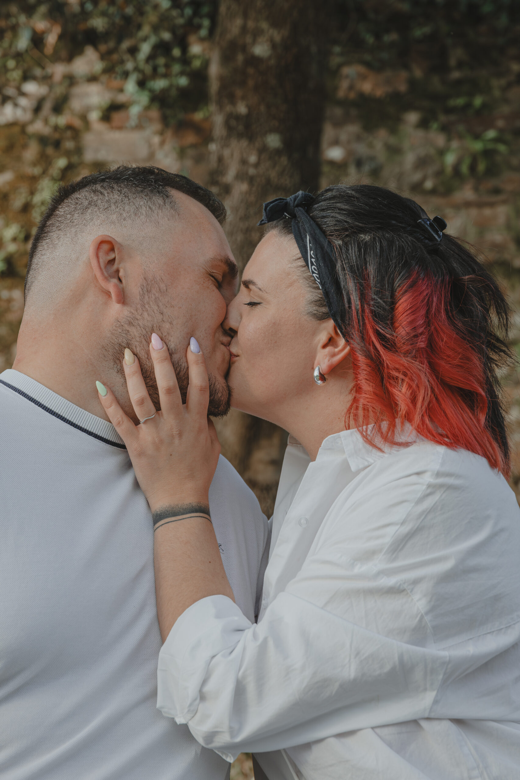 Femme tenant le visage de son futur mari en l'embrassant, mettant en valeur sa bague de fiançailles, lors d’une séance photo engagement au Parc des Remparts à Montaigu-Vendée en Vendée, réalisée par Solène photographe.