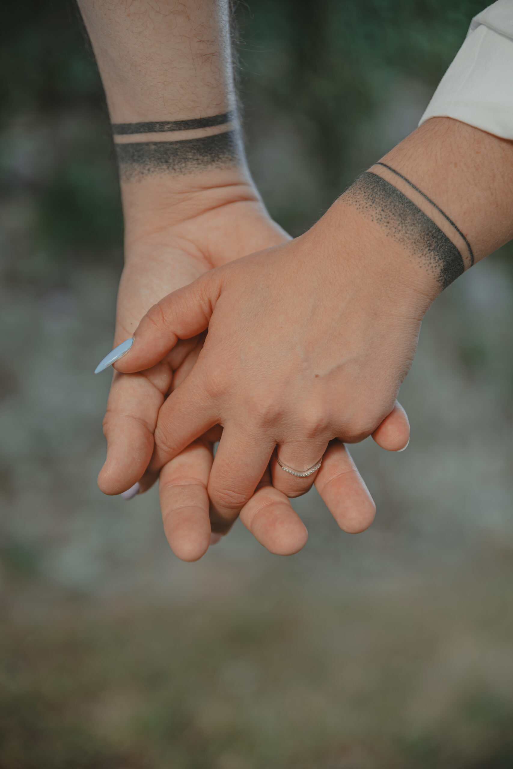 Zoom sur des mains enlacées, mettant en valeur leurs tatouages communs et la bague de fiançailles, lors d’une séance photo engagement au Parc des Remparts à Montaigu-Vendée en Vendée, réalisée par Solène photographe.