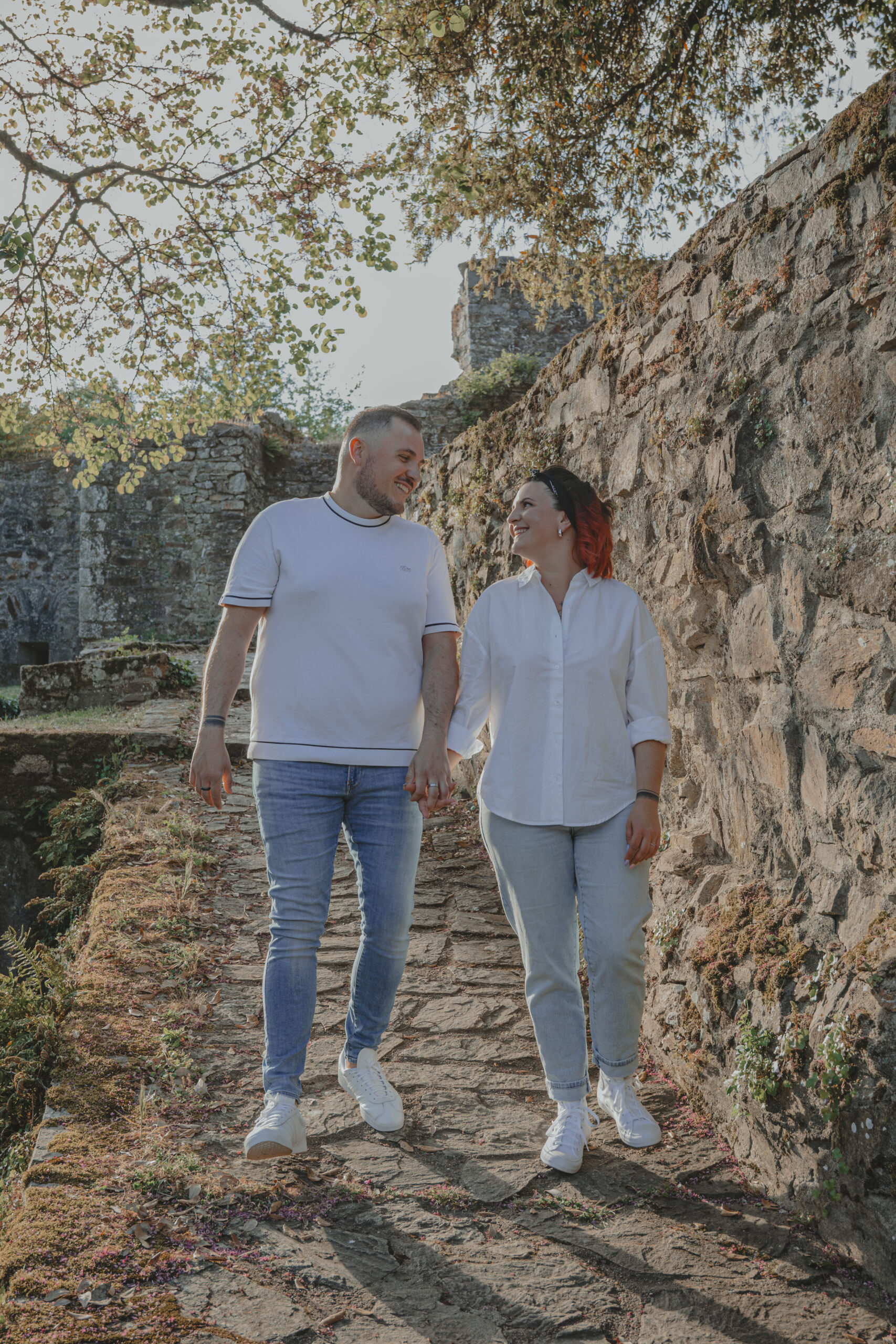 Couple marchant en se regardant et en se donnant la main, lors d’une séance photo engagement au Parc des Remparts à Montaigu-Vendée, réalisée par Solène photographe.