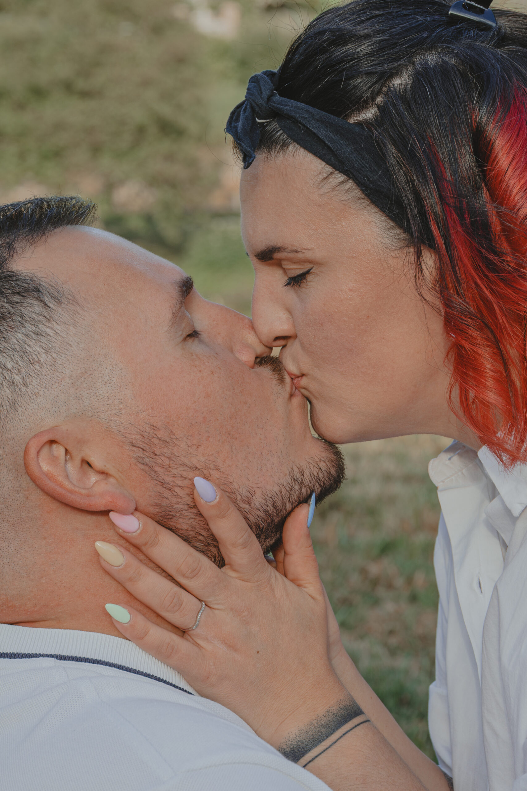 Femme tenant dans ses mains le visage de son futur mari en l'embrassant, mettant en valeur sa bague de fiançailles, lors d’une séance photo engagement au Parc des Remparts à Montaigu-Vendée, réalisée par Solène photographe.